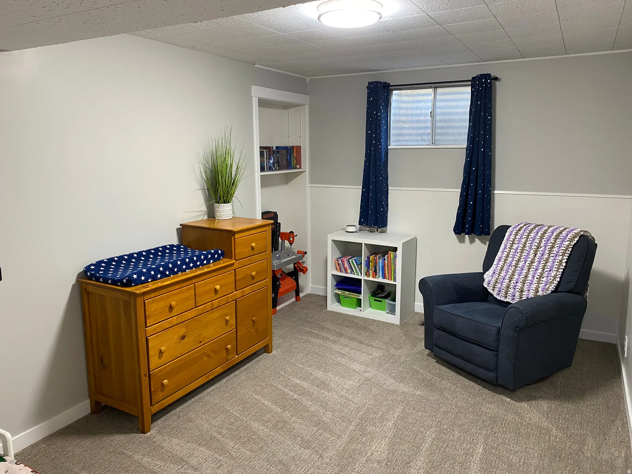Carpeted room featuring a drop ceiling with recessed lighting, light gray walls with white wainscoting, and a built-in wall niche with shelving