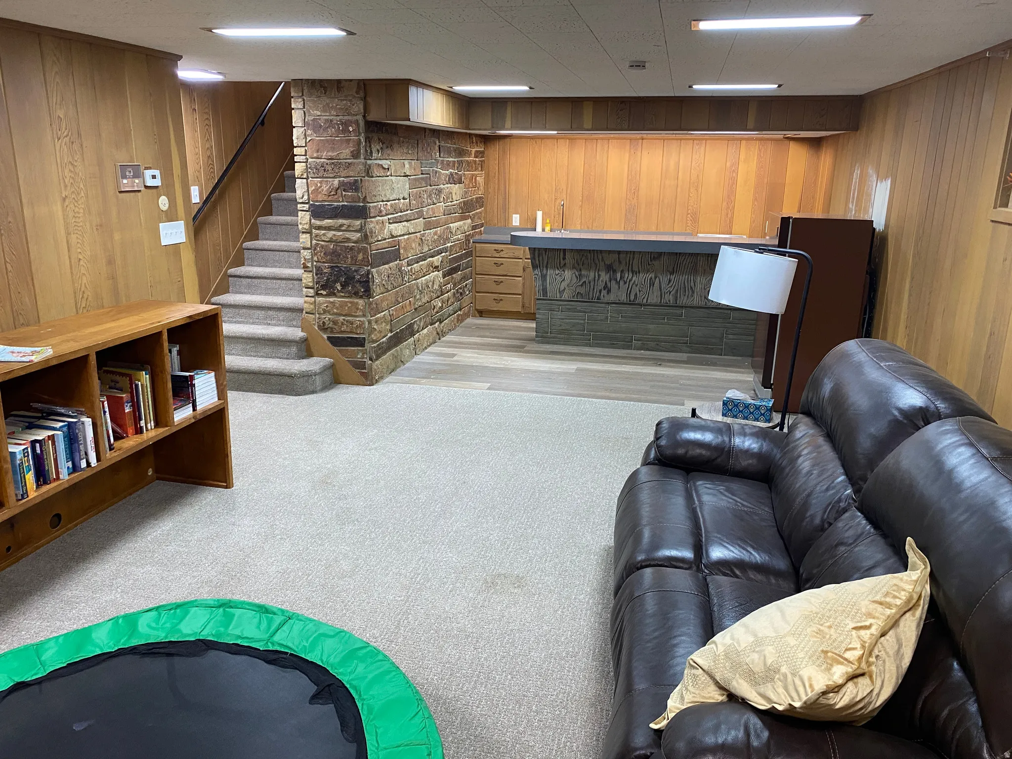 Spacious lower level featuring wood paneling, a built-in wet bar with a gray countertop, and a carpeted staircase with a stone accent wall