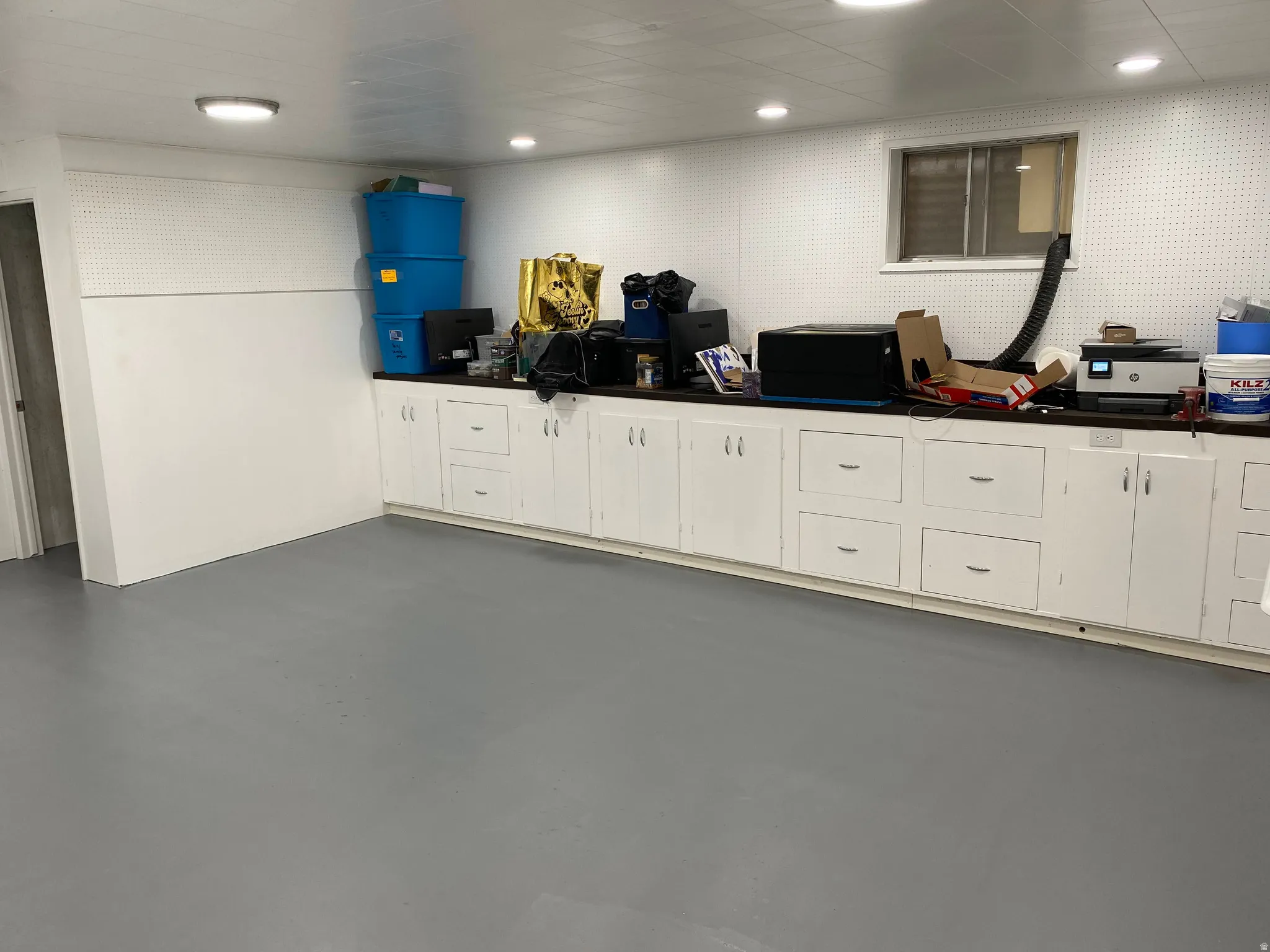 Spacious utility room featuring extensive white cabinetry with dark countertops, grey flooring, and recessed lighting
