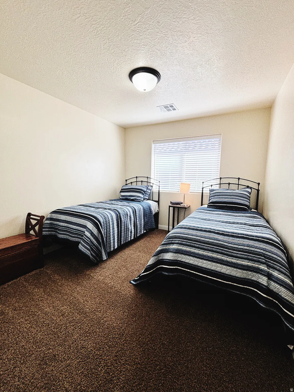 Carpeted interior room featuring light-toned walls, a textured ceiling, and a flush-mount ceiling light fixture