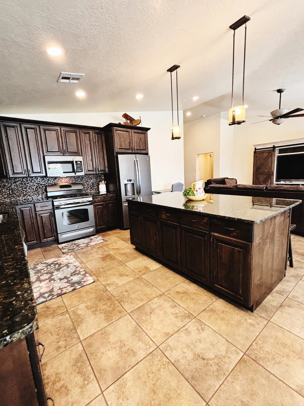 Expansive kitchen featuring dark wood cabinetry, stainless steel appliances, and a central island with granite countertops