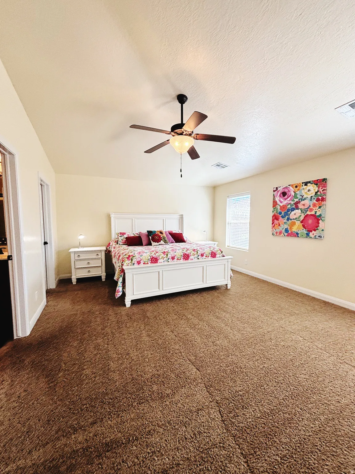 Spacious bedroom featuring neutral-toned walls, brown carpet flooring, and a ceiling fan with integrated lighting