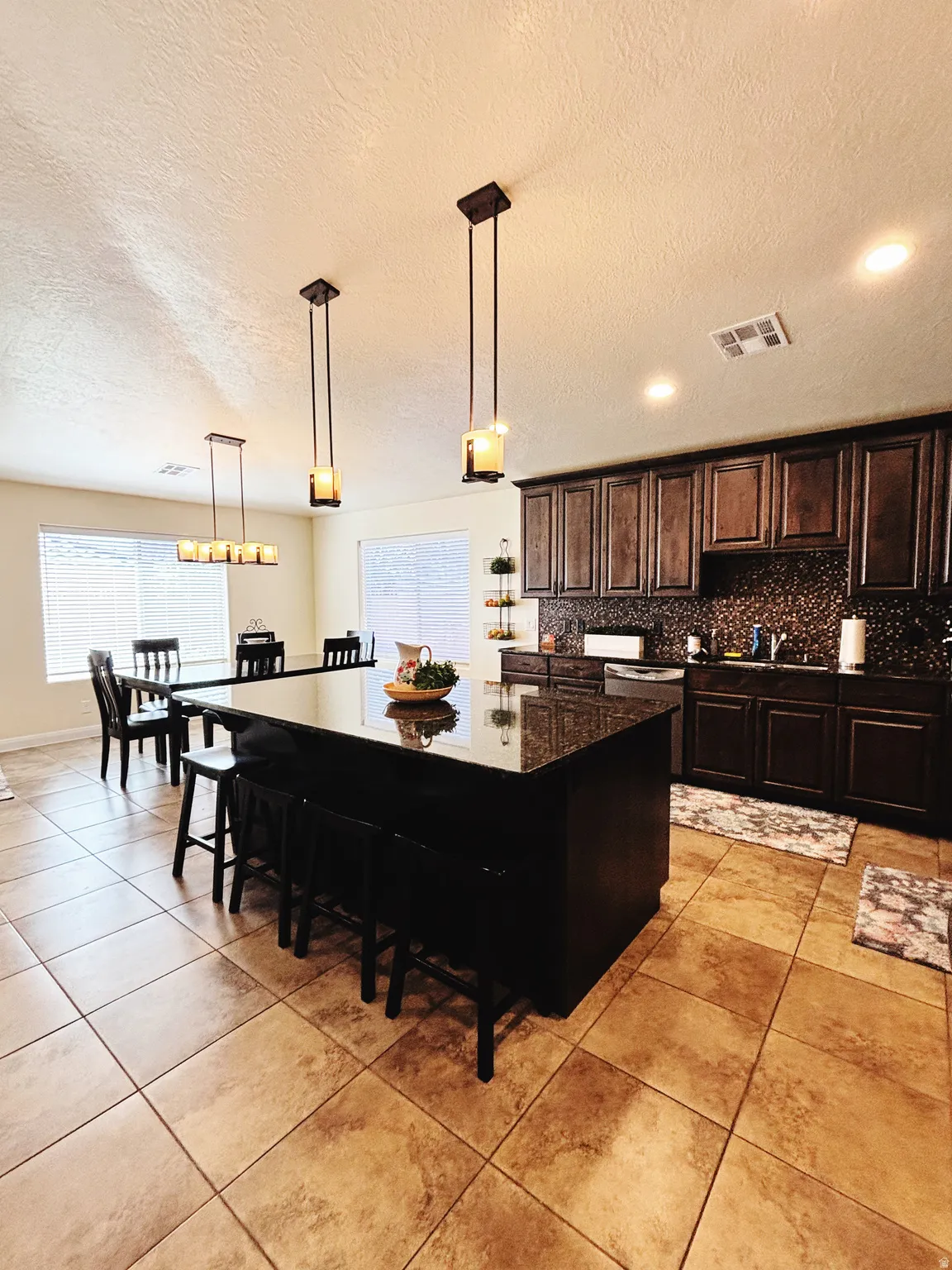 Kitchen featuring a large island with a dark countertop and seating, dark wood-finish cabinetry, a mosaic tile backsplash, and recessed lighting