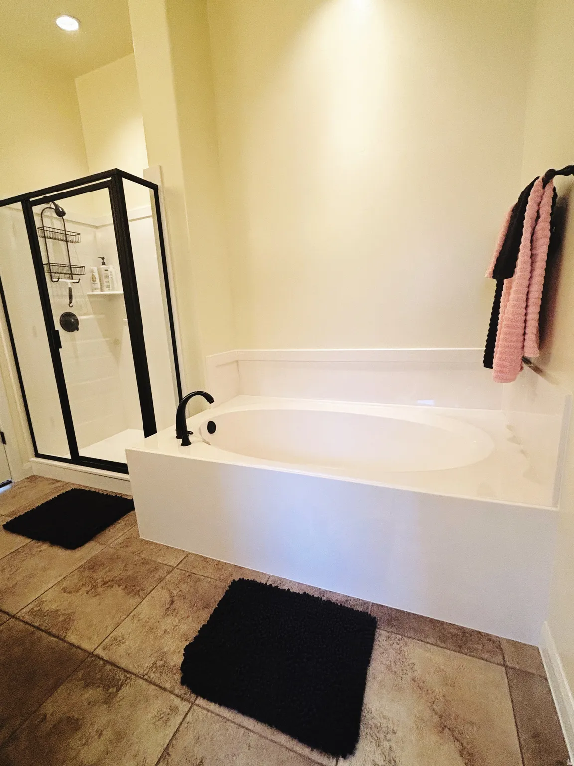 Soaking tub with matte black fixtures, complemented by a glass-enclosed shower with black trim, and tile flooring