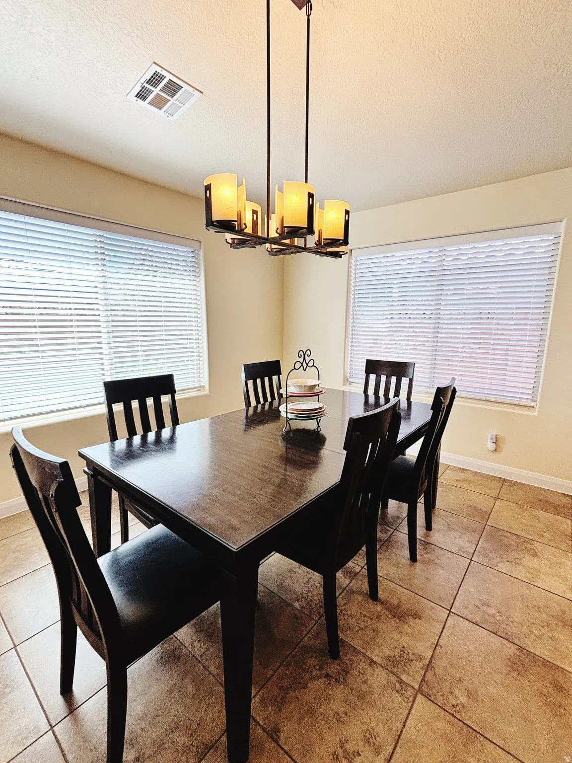 Dining area featuring a contemporary chandelier, two windows with horizontal blinds, and large format tile flooring