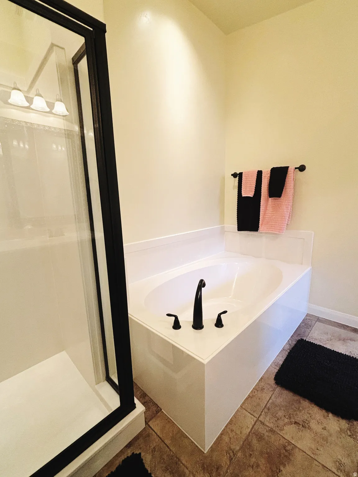 Bathroom featuring an alcove bathtub with matte black fixtures, a separate shower with a black-framed glass enclosure, and tiled flooring