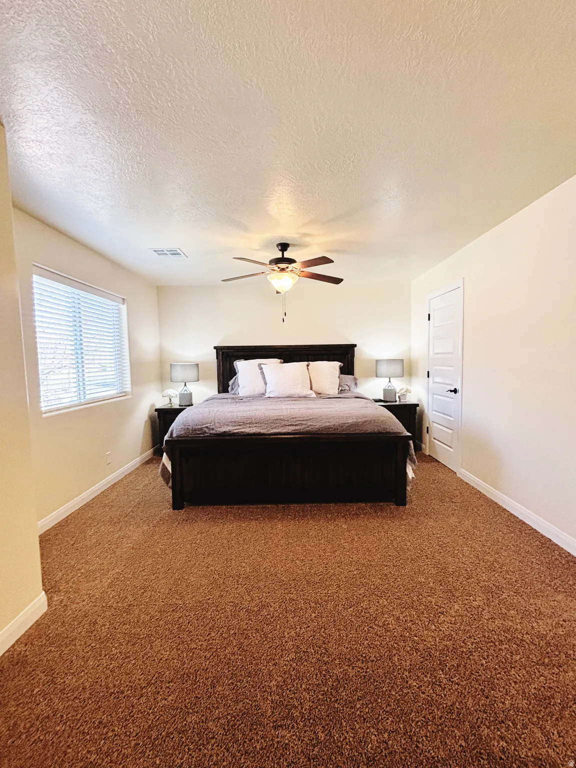 Spacious room with a ceiling fan light fixture, light beige walls, and brown carpet flooring