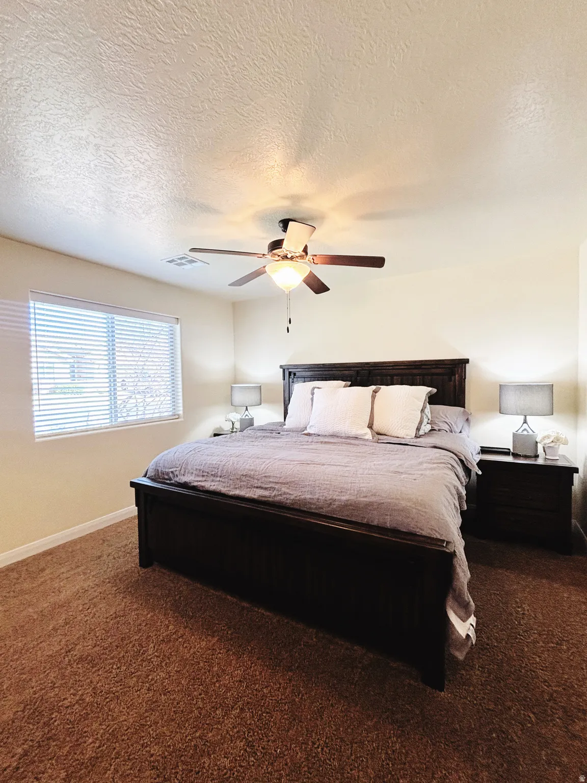 Expansive room featuring warm-toned carpet flooring, a large window with horizontal blinds, and a ceiling fan with integrated lighting