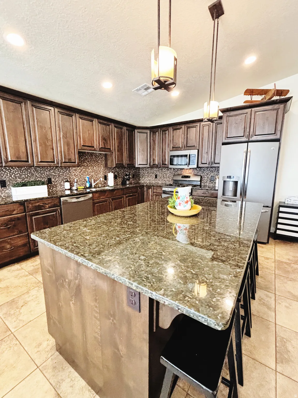 Kitchen featuring a large island with stone countertop, wood-finish cabinetry, tile flooring, stainless steel appliances, and recessed lighting