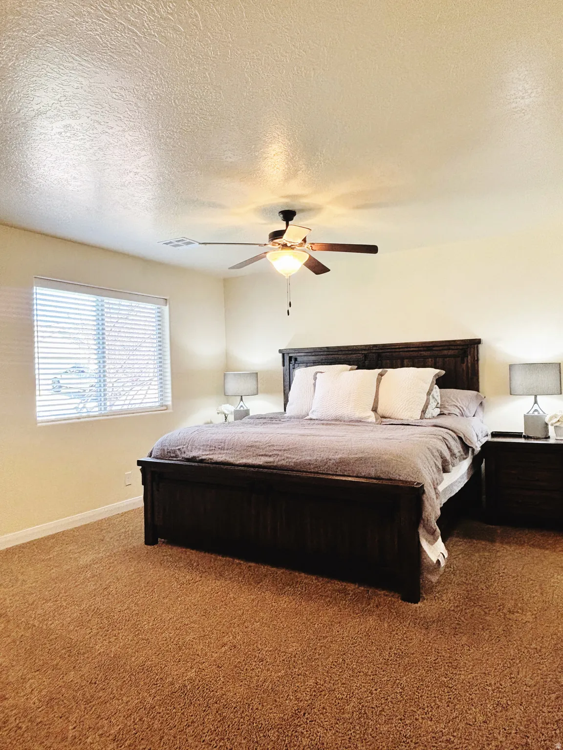 Carpeted bedroom featuring a window with horizontal blinds, a ceiling fan with integrated lighting, and painted walls