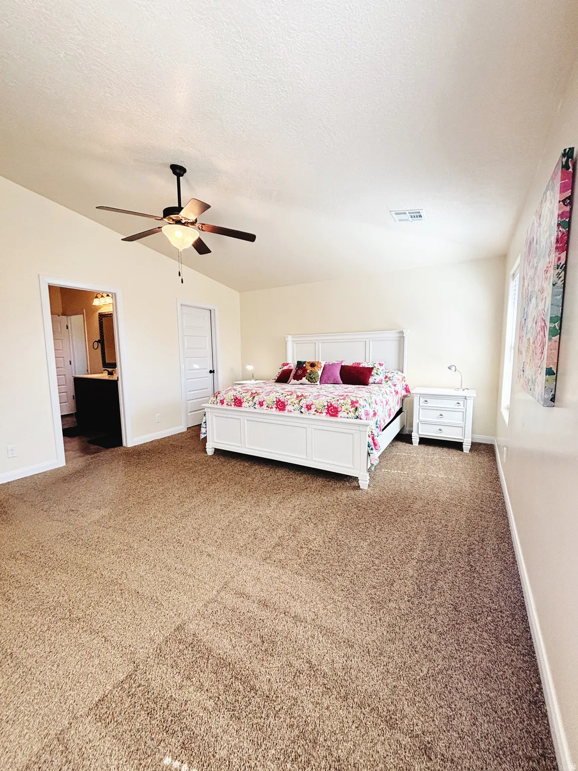 Carpeted bedroom featuring a ceiling fan with integrated lighting, neutral wall tones, a white paneled door, and an open doorway to an adjoining space