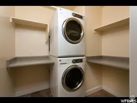Utility area featuring light beige walls, a stacked washer and dryer, and built-in shelving