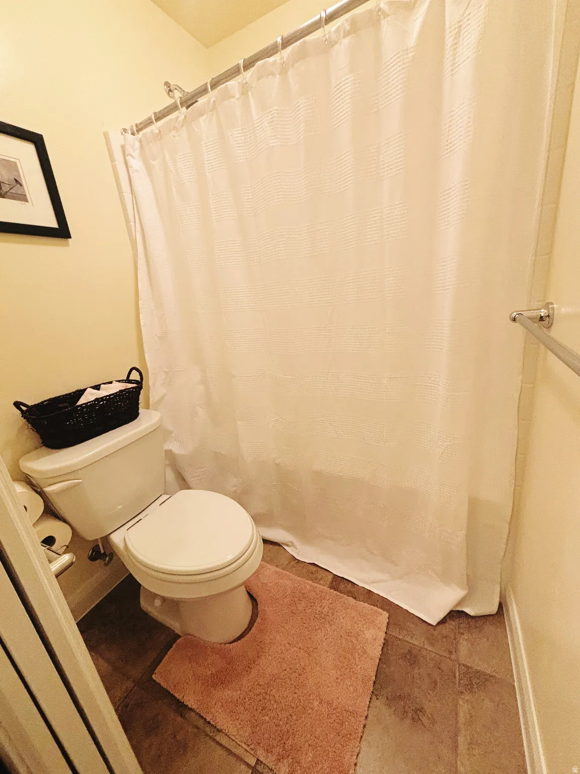 Bathroom featuring a shower/tub combination with a chrome shower rod, toilet, and tile flooring