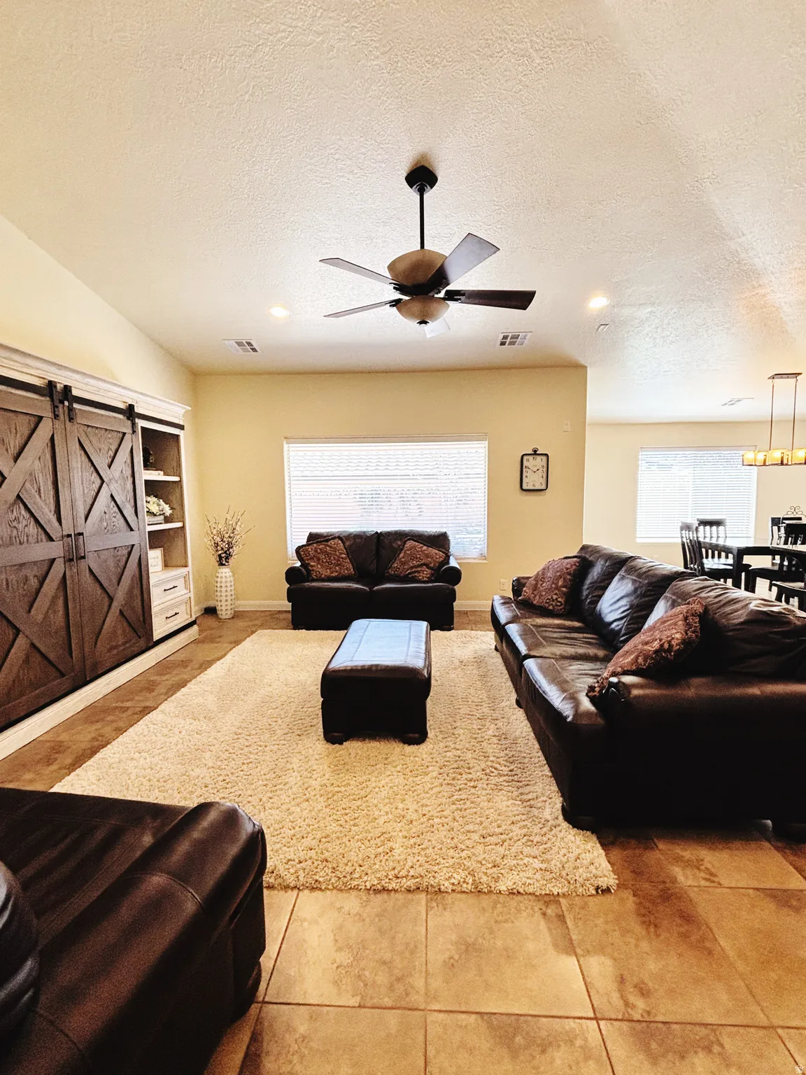 Spacious living area featuring tile flooring, built-in cabinetry with barn doors, recessed lighting, a ceiling fan, and multiple windows