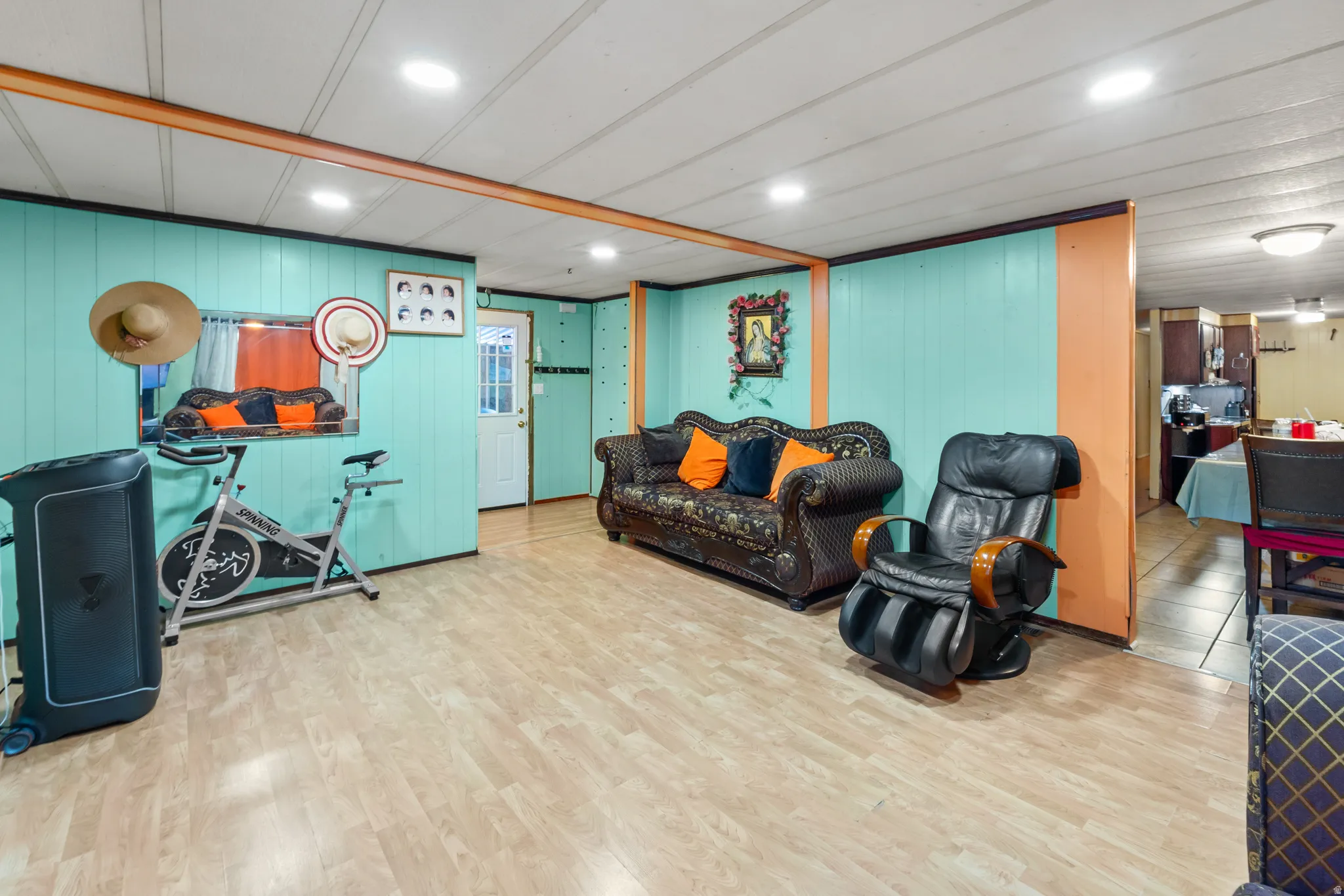 Spacious room featuring light wood-finish flooring, a white paneled ceiling with recessed lighting, and bright turquoise wall paneling