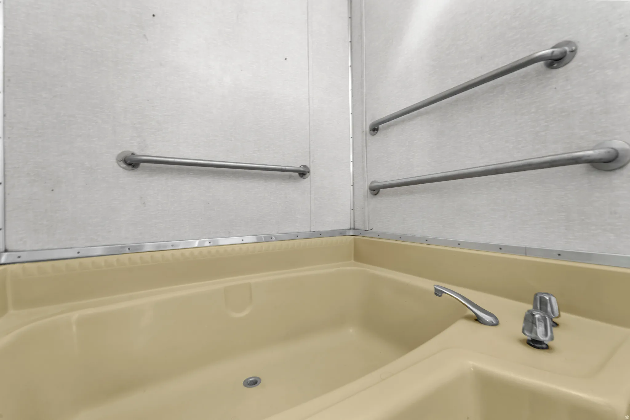 Beige garden tub with chrome fixtures, surrounded by white paneling and metal grab bars