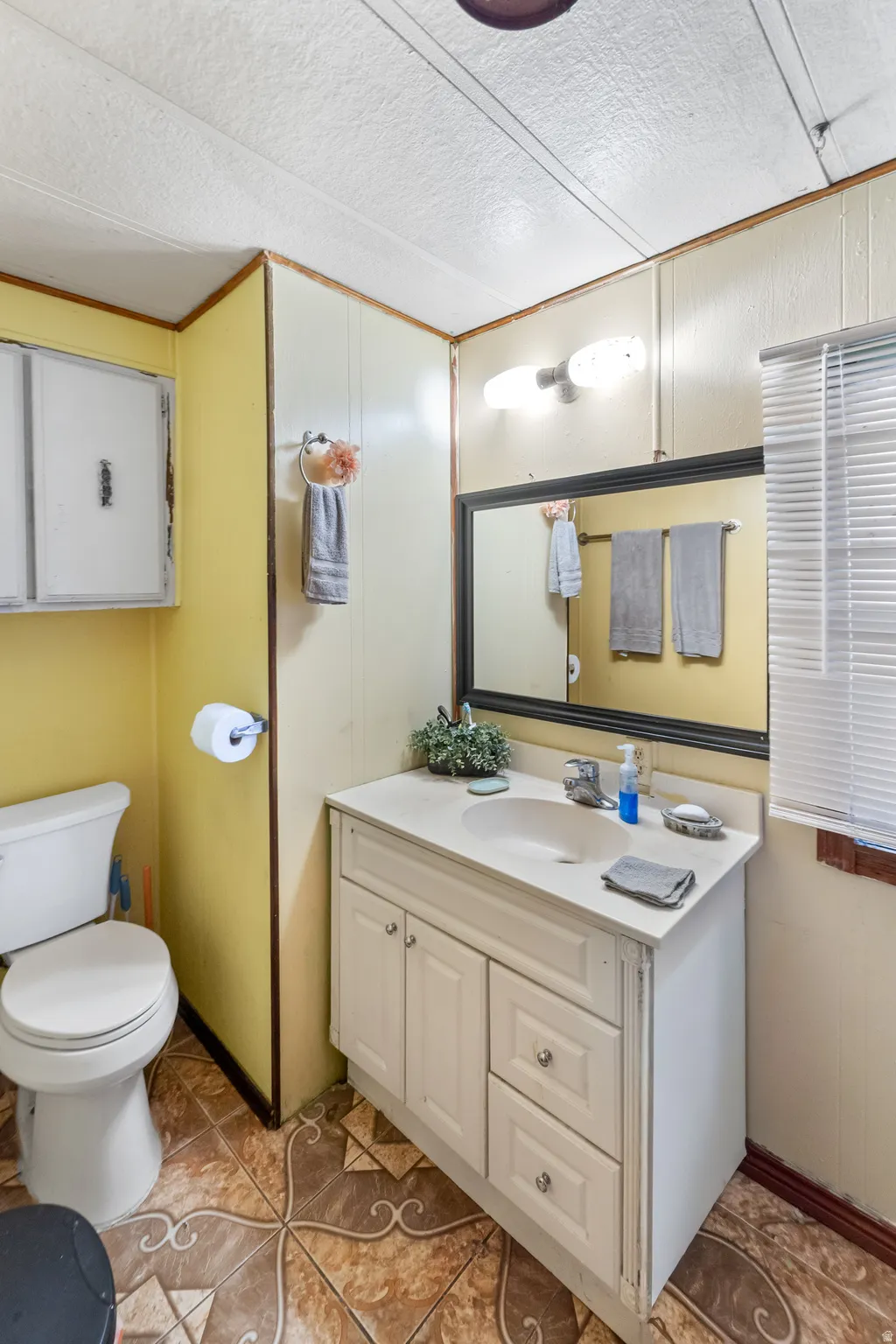 Bathroom featuring a white vanity with integrated sink, a rectangular framed mirror, dual-bulb vanity lighting, and patterned floor tiling