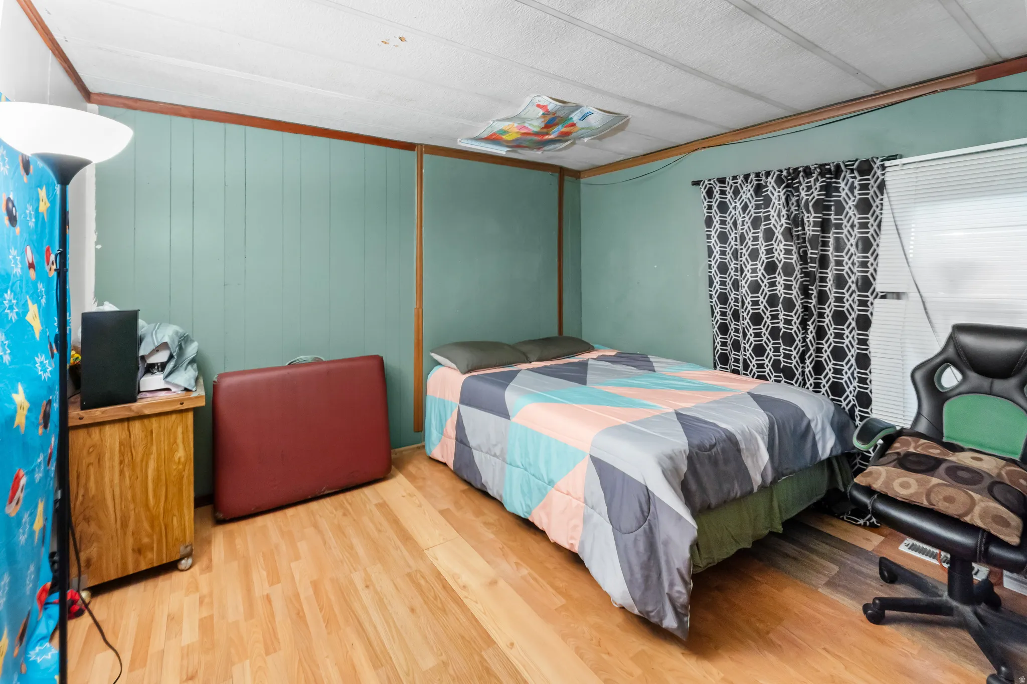 Interior room featuring wood-finish flooring, light teal wall paneling, and a large window with horizontal blinds