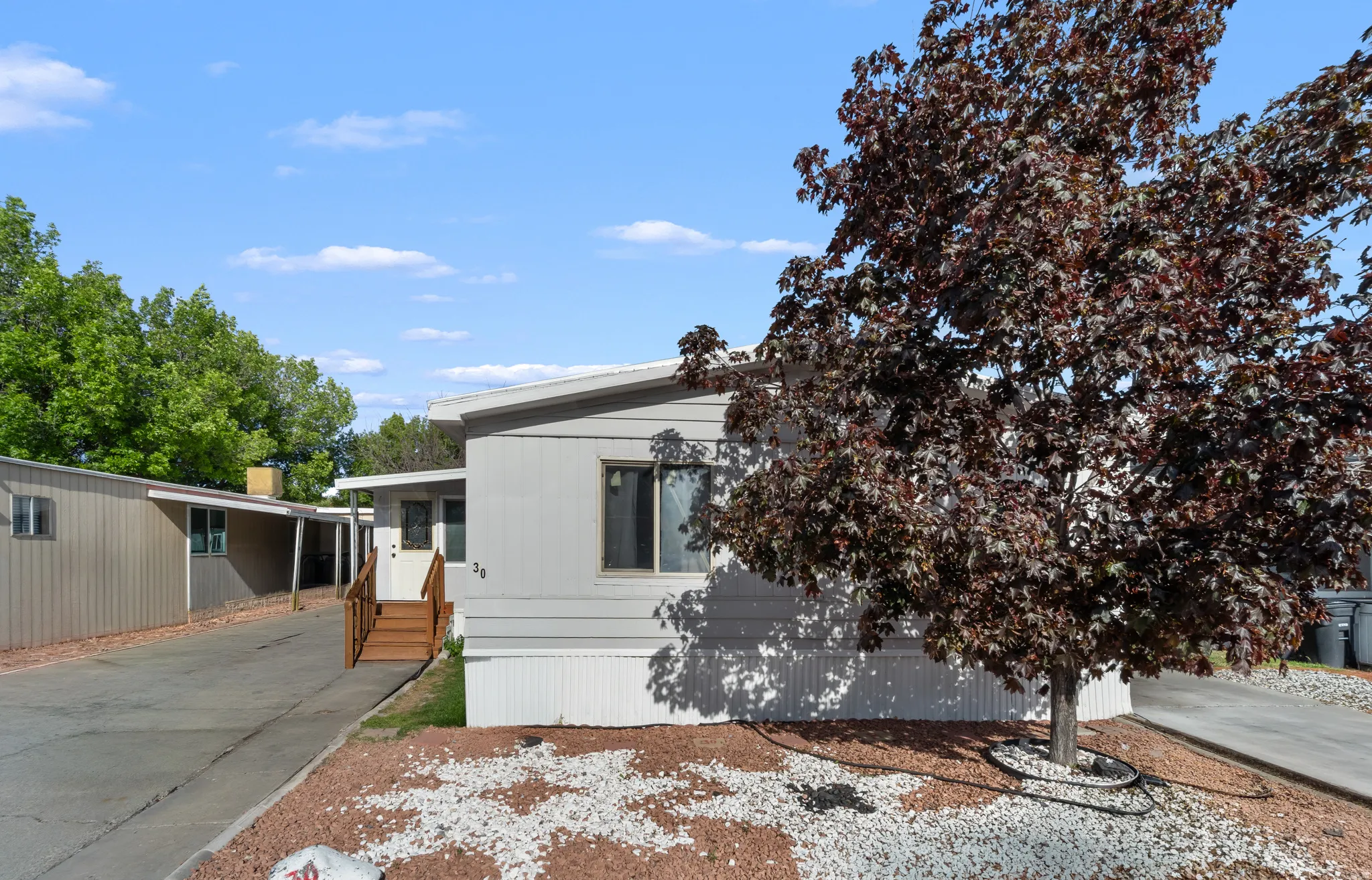 Light grey manufactured home with a white trim roof and white skirting