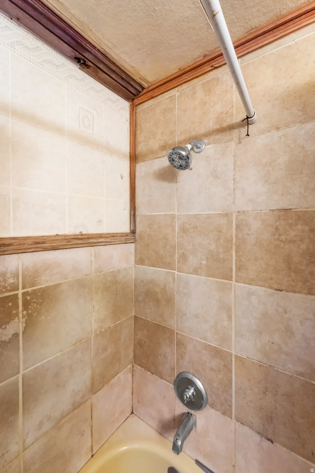 Tub and shower surround featuring earth-toned square tiles and a chrome shower head with a matching faucet