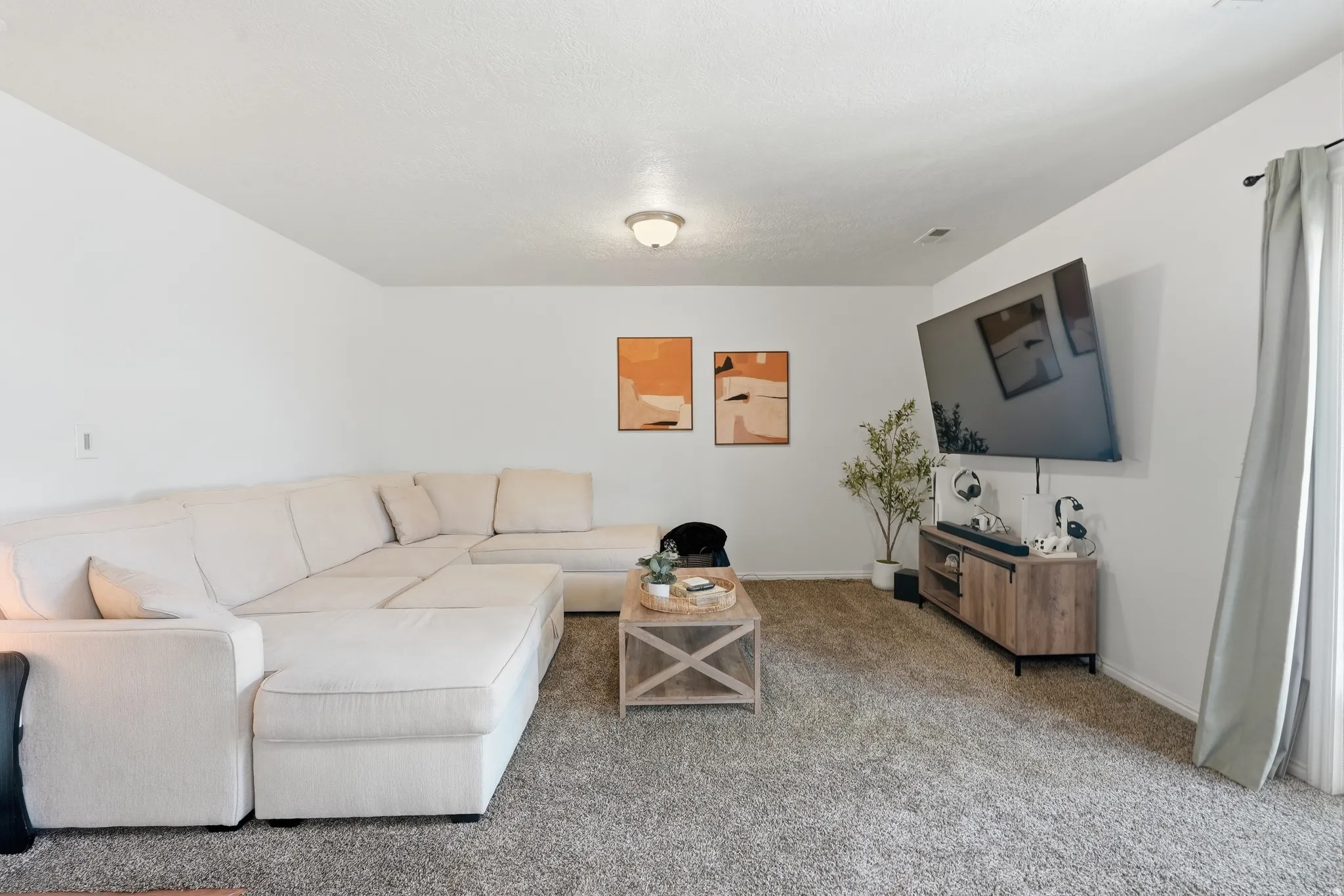 Spacious living area featuring neutral carpeting, white walls, and a ceiling-mounted light fixture