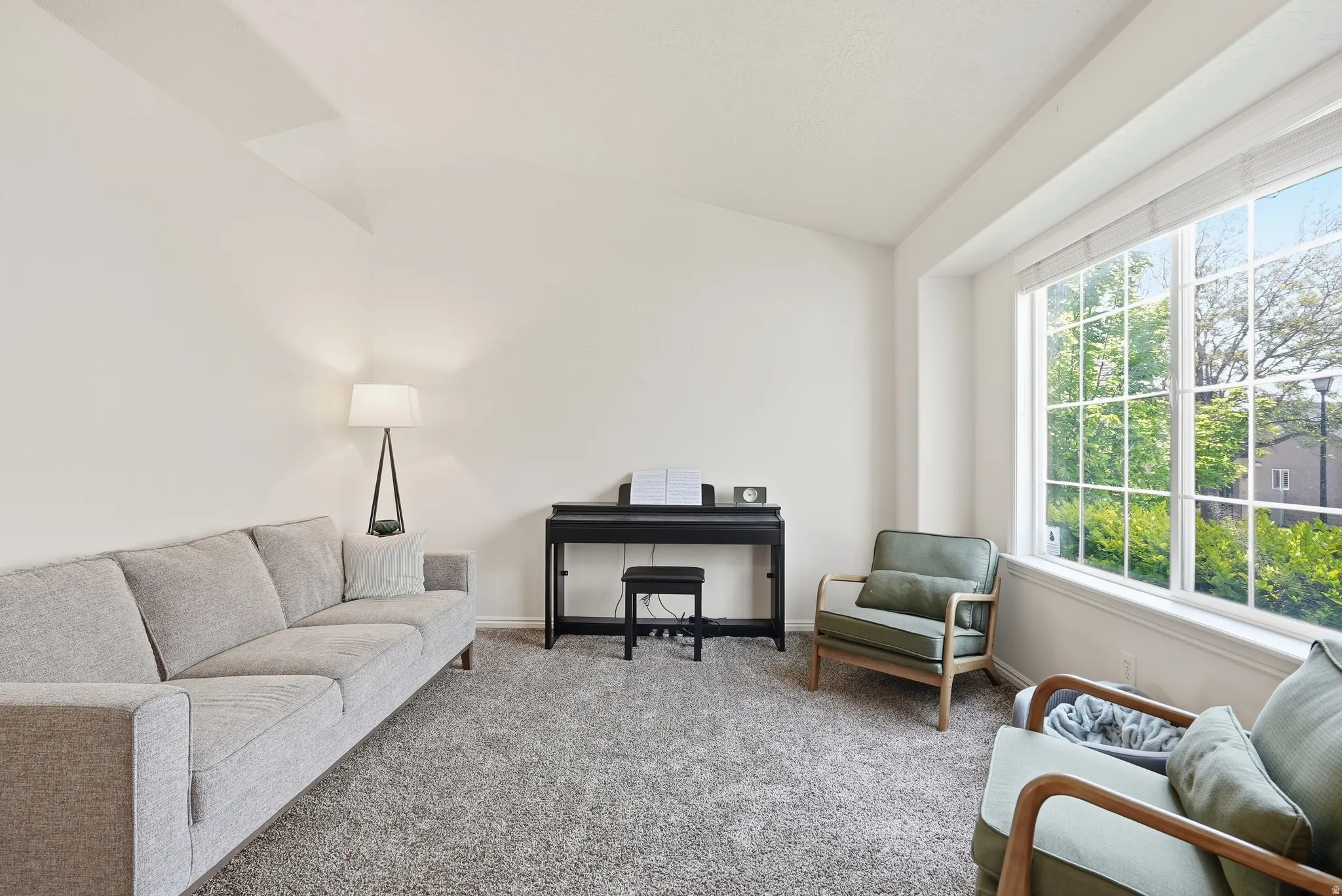 Room featuring a large window with multiple panes and white blinds, light-toned walls, and a vaulted ceiling