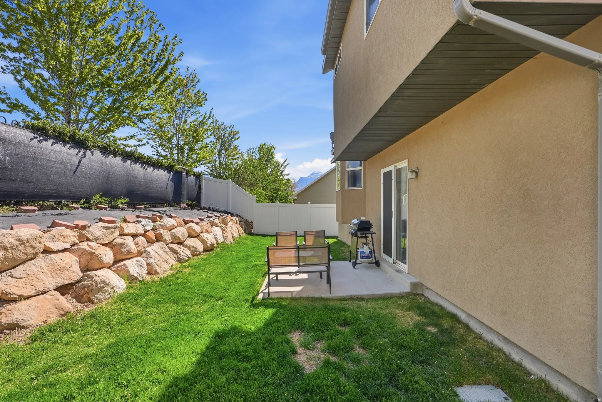 Exterior patio with sliding glass door access, surrounded by a rock retaining wall, privacy fencing, and mature trees