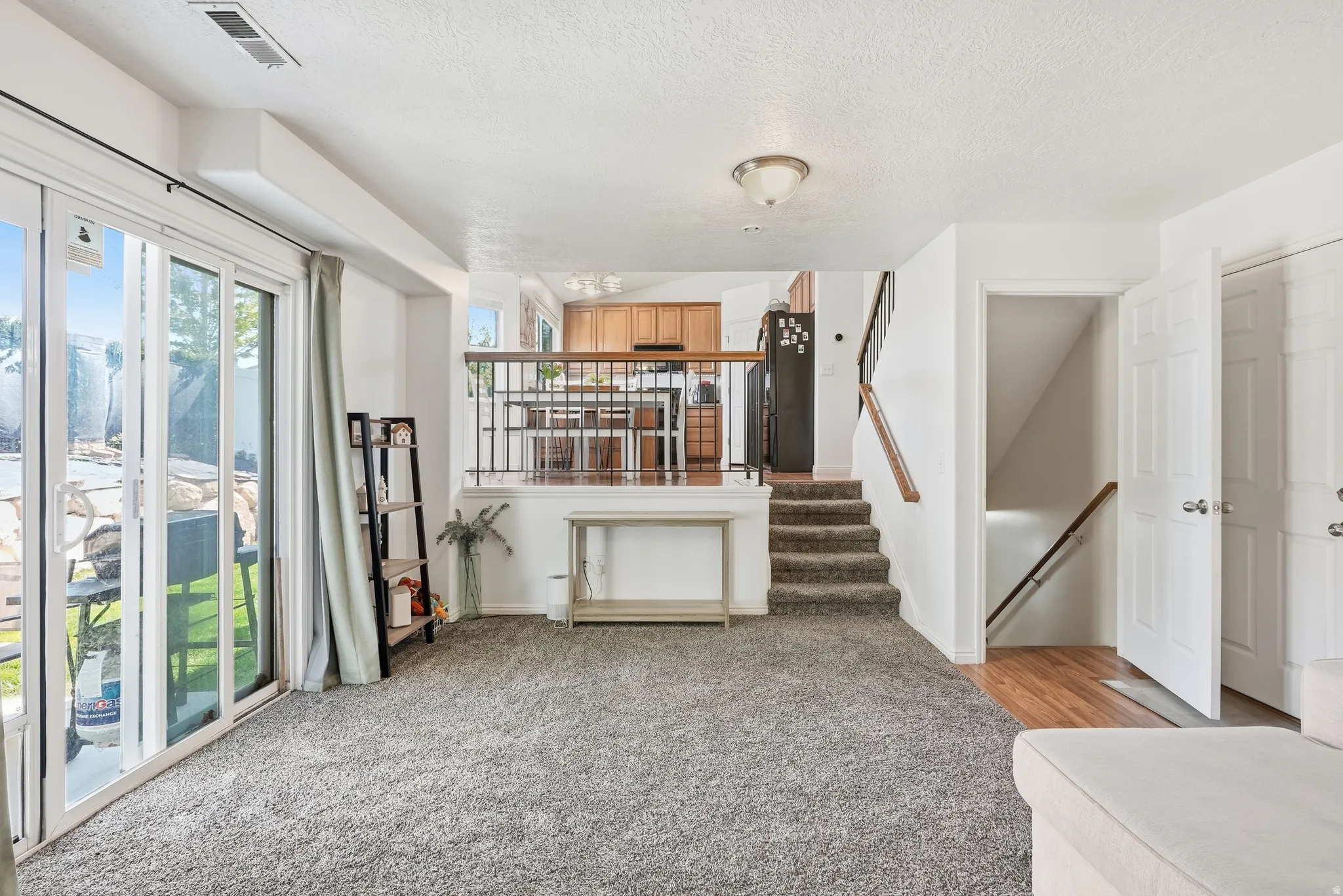 Spacious living area featuring plush gray carpeting, white walls, and a sliding glass door offering outdoor access