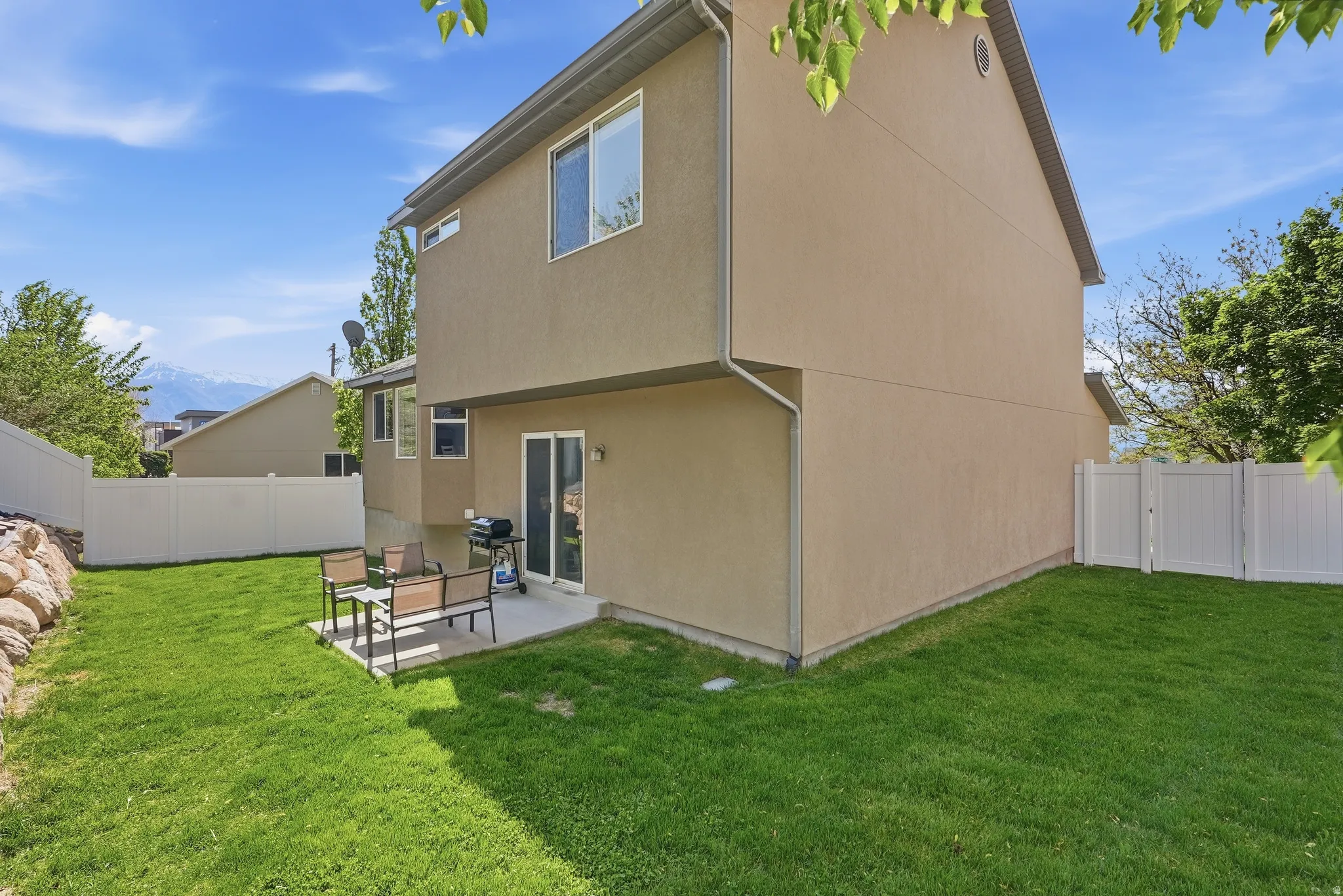 Expansive green lawn with a concrete patio, featuring sliding glass doors and a privacy fence