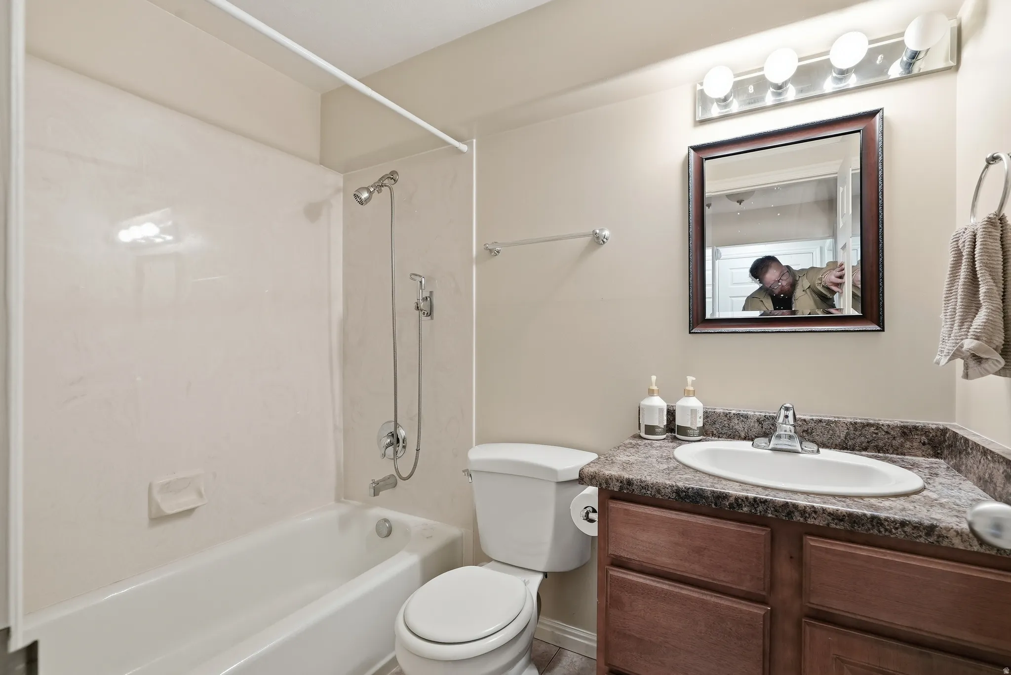 Bathroom featuring a tub/shower combination with a bright white surround, a chrome showerhead with an attached handheld sprayer, a wood-finish vanity with cabinet storage, a speckled countertop, and an oval undermount sink with a chrome faucet