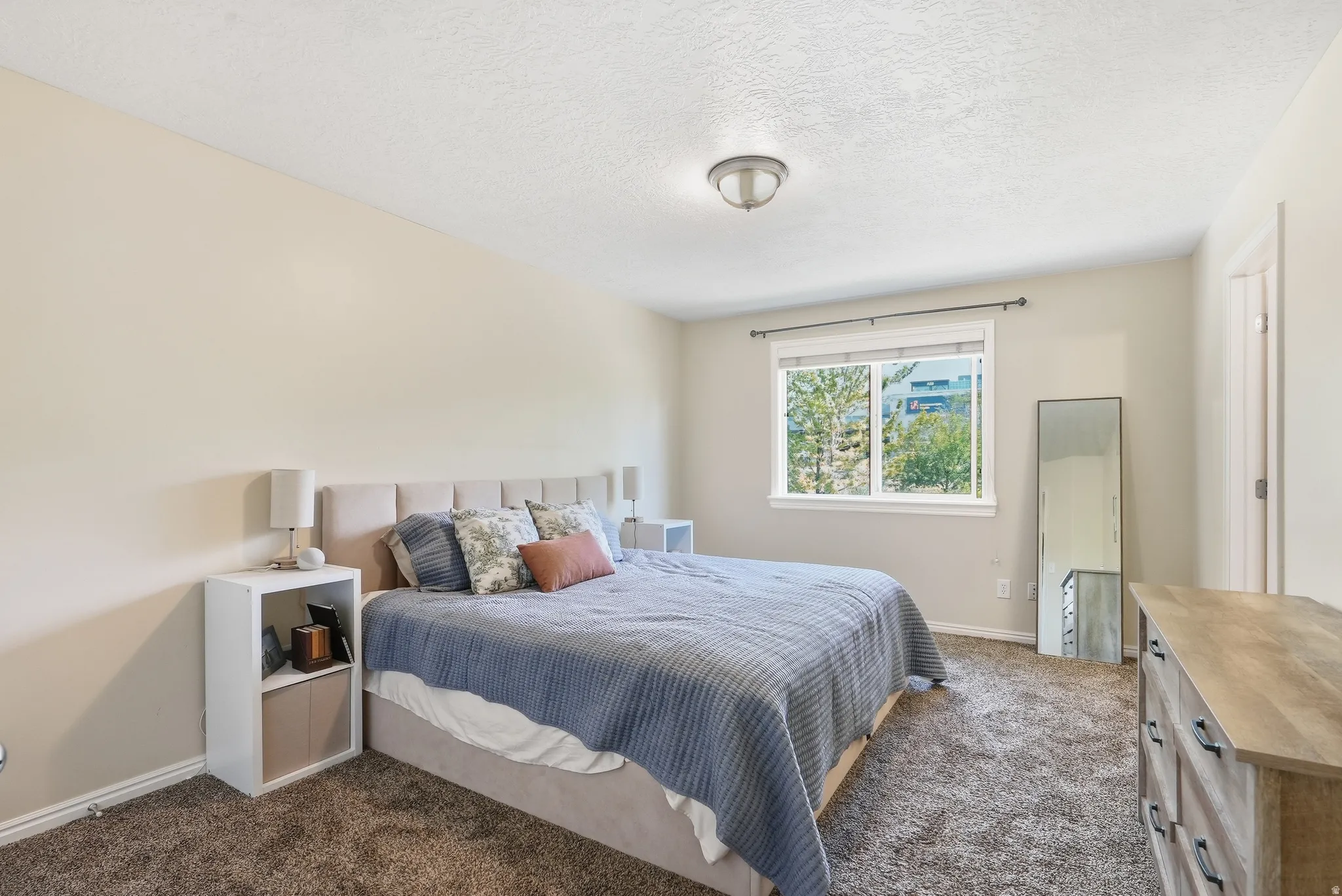 Carpeted bedroom featuring a large window with white trim, a flush-mount ceiling light fixture, and light-colored walls