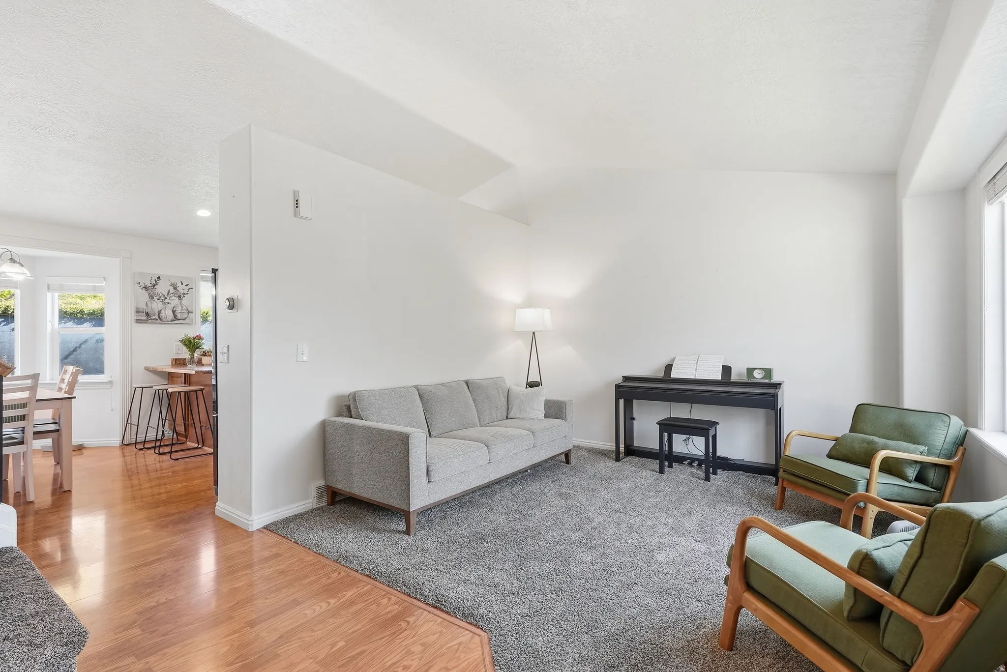 Carpeted living area with abundant natural light, featuring a half-wall partition and wood-finish flooring in the dining space