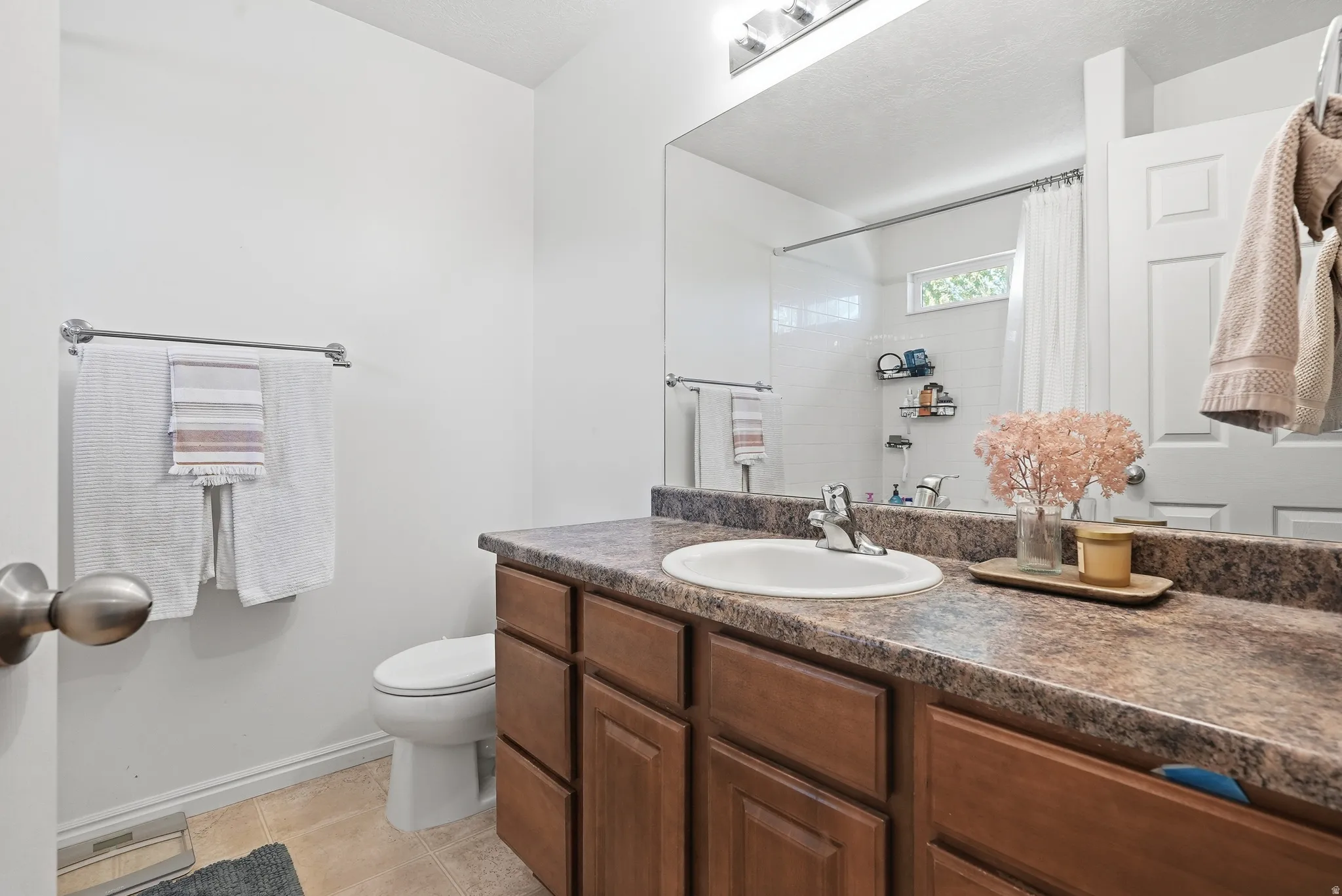 Bathroom featuring a wood-finish vanity with a built-in sink, a speckled countertop, and a large wall mirror