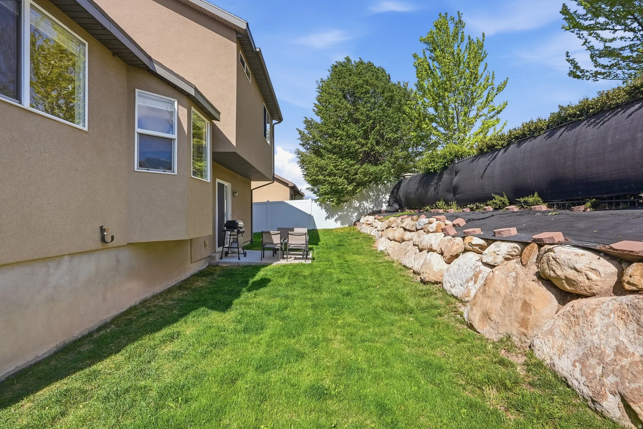 Expansive lawn area featuring a stone retaining wall and mature trees