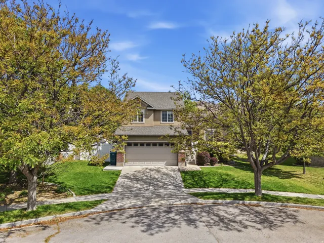 Two-story residence featuring a two-car garage, established front yard landscaping, and a sloped driveway