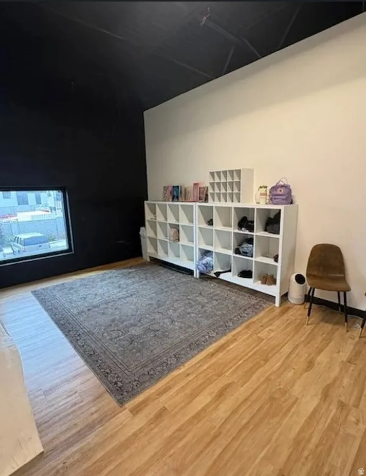 Spacious room featuring wood-finish flooring, a large window, high ceilings, and neutral-toned walls