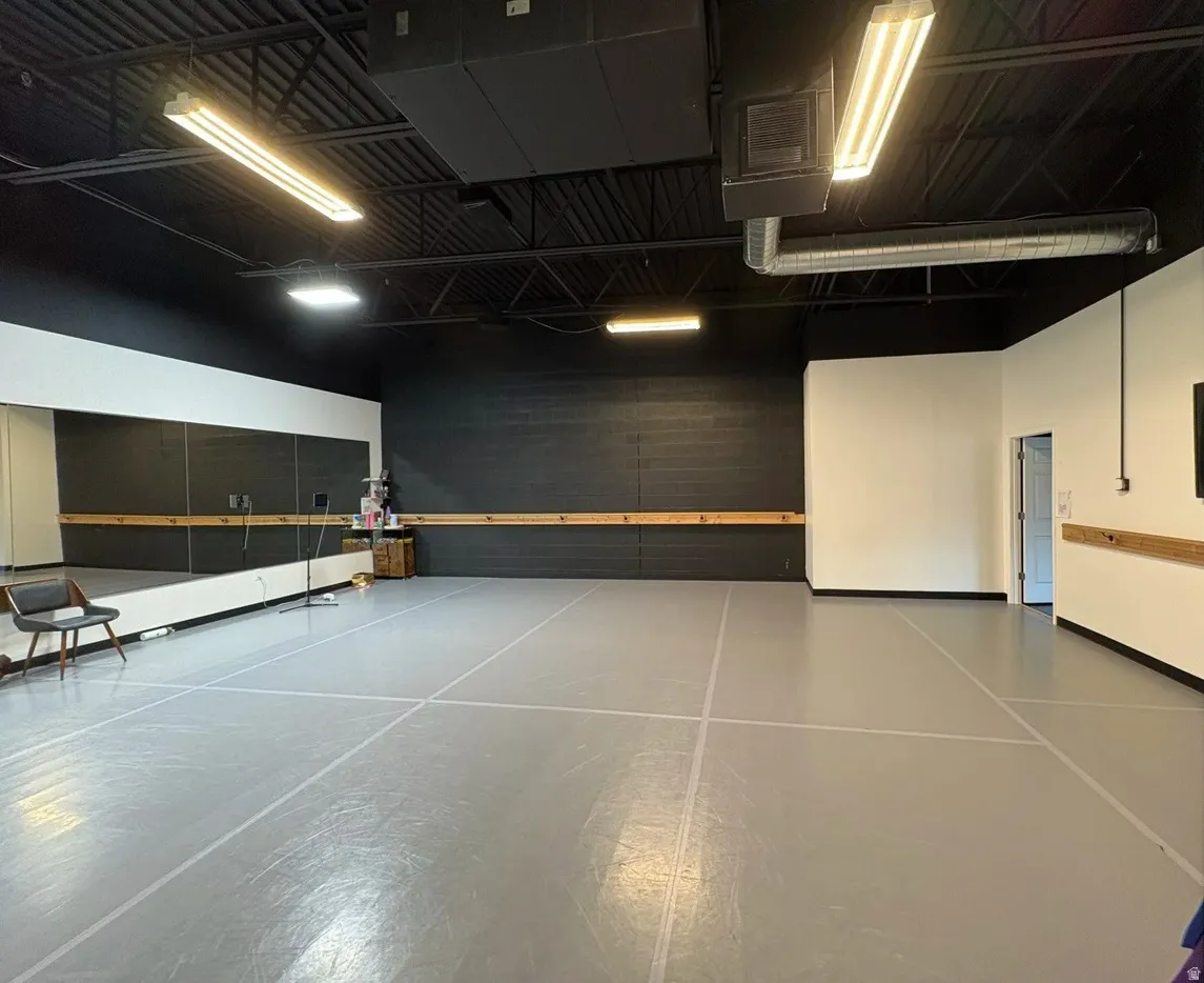 Spacious commercial interior featuring high ceilings with exposed ductwork, fluorescent lighting, and durable gray flooring