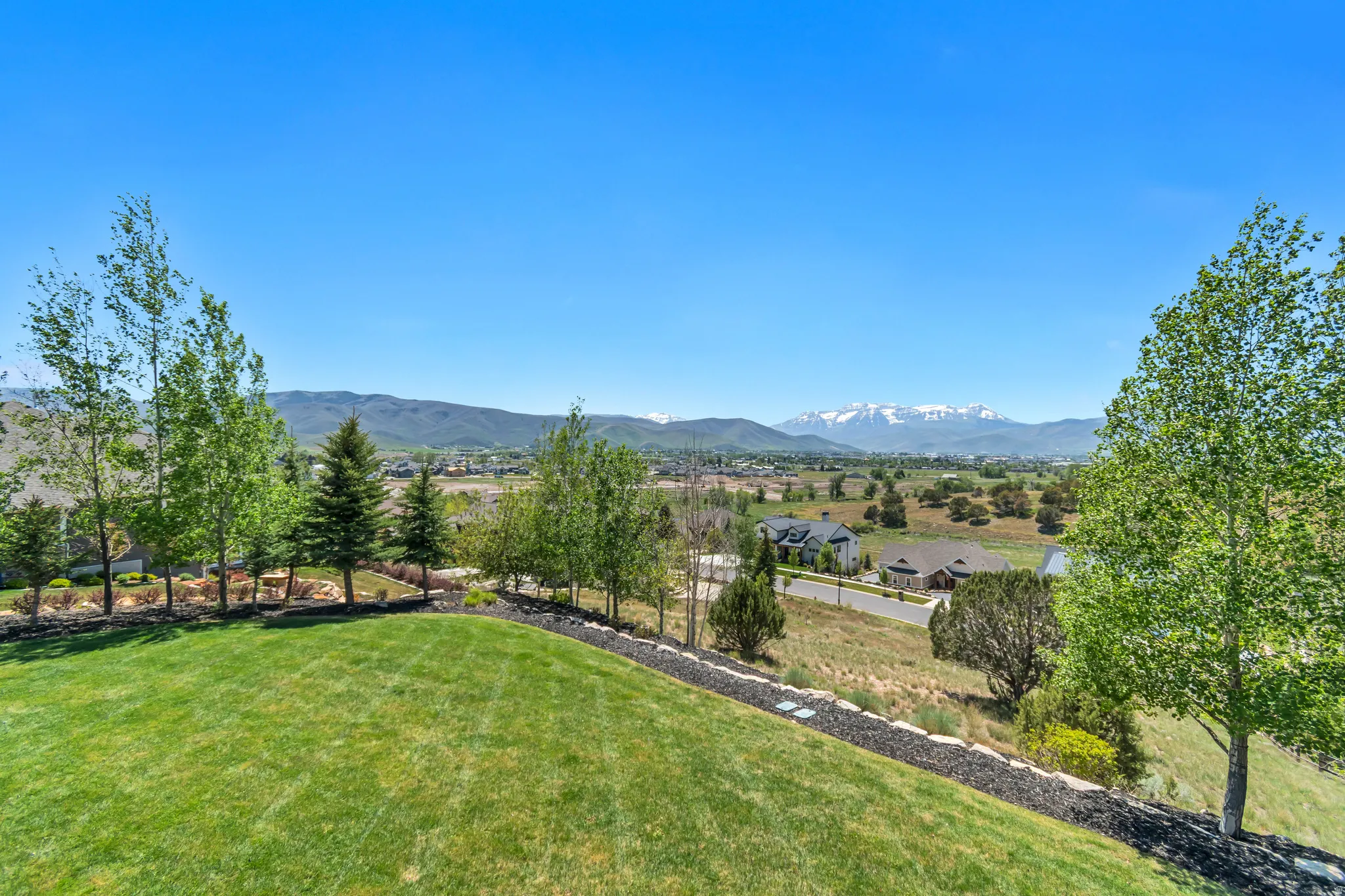 Expansive green lawn with mature trees and a distant mountain range featuring snow-capped peaks