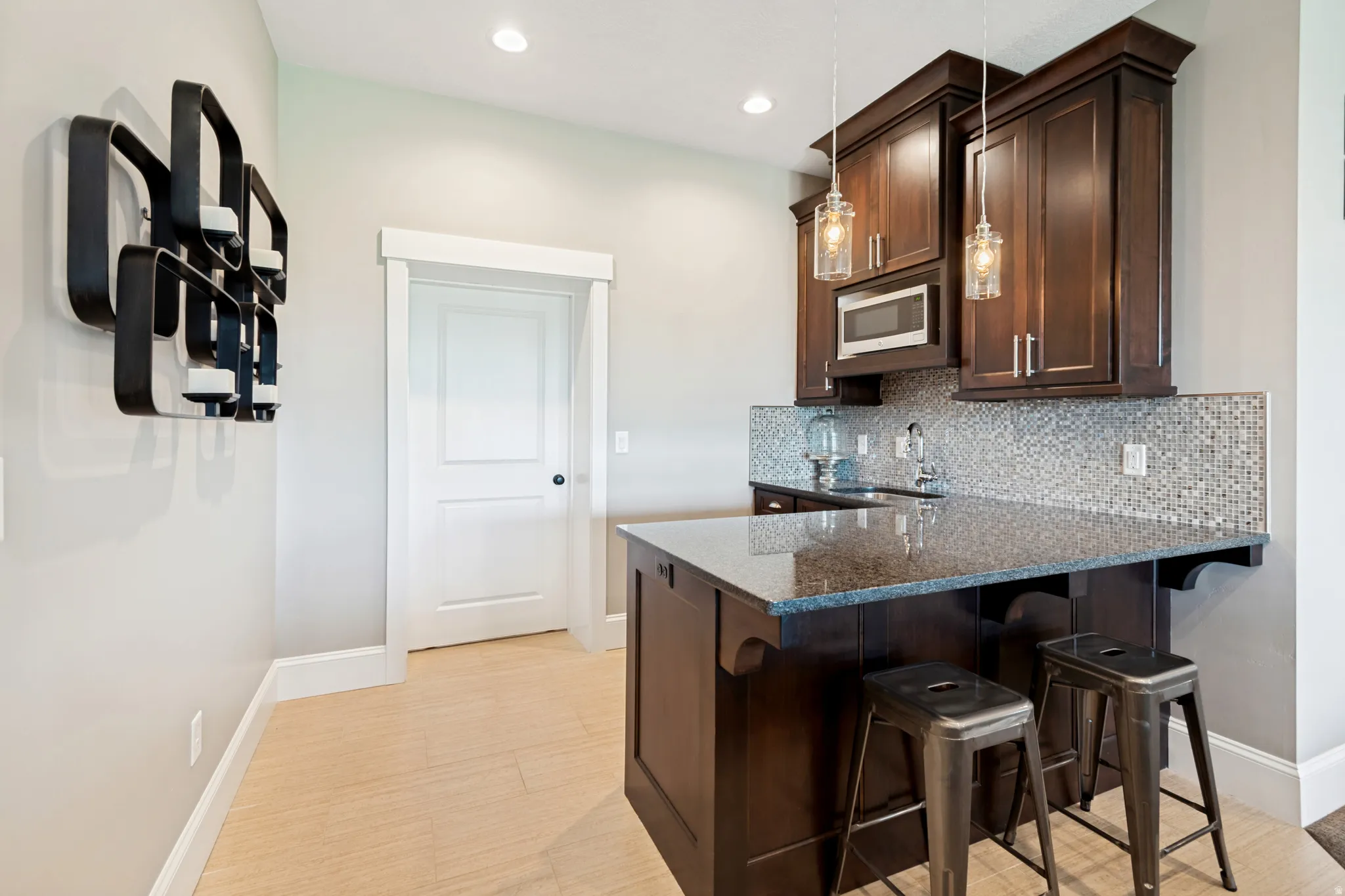 Built-in wet bar featuring dark wood cabinetry, a microwave, mosaic tile backsplash, and a polished countertop with seating
