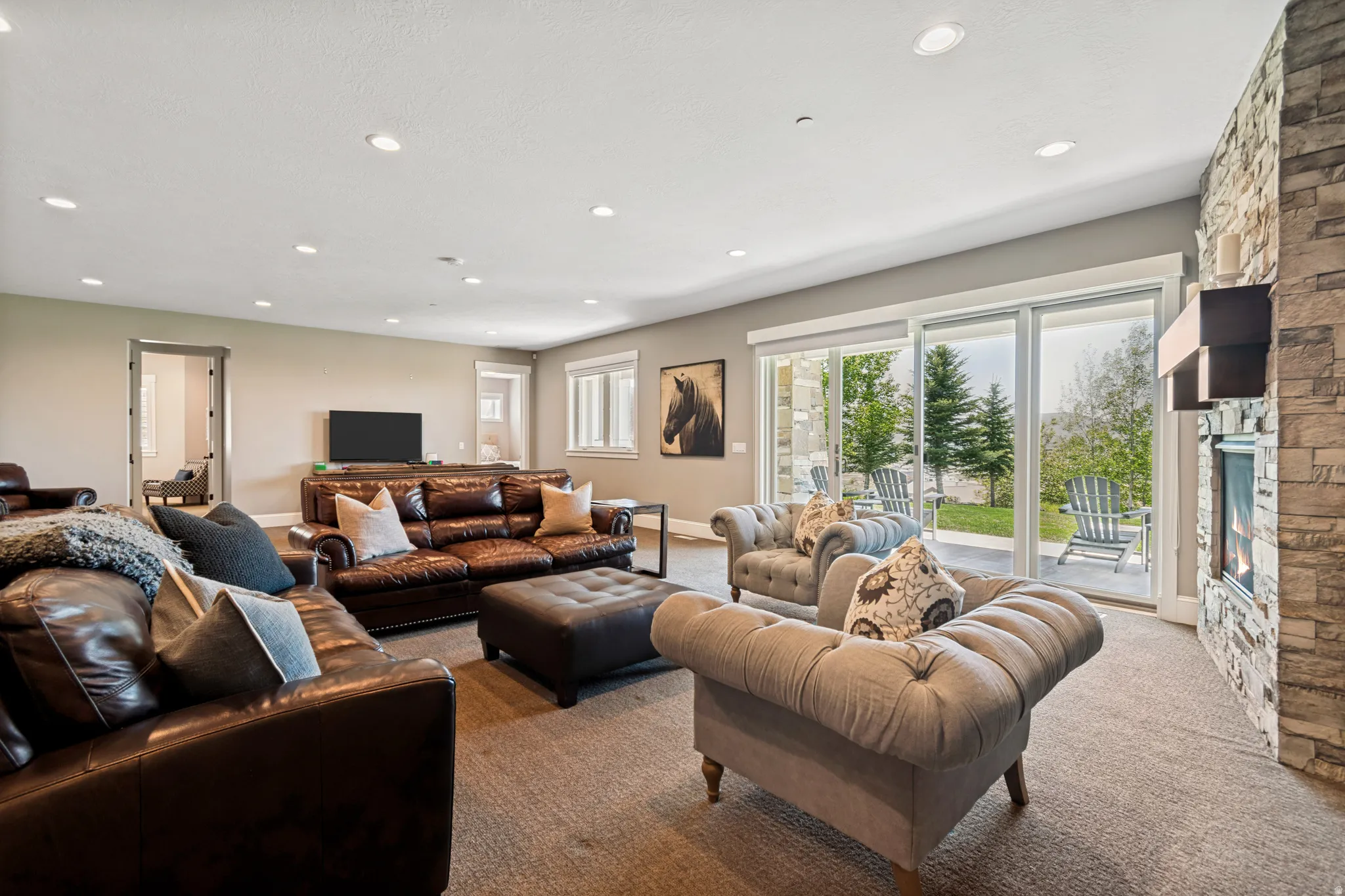 Spacious living area featuring a stone-clad fireplace with a modern mantle, recessed lighting, and sliding glass doors opening to the exterior patio