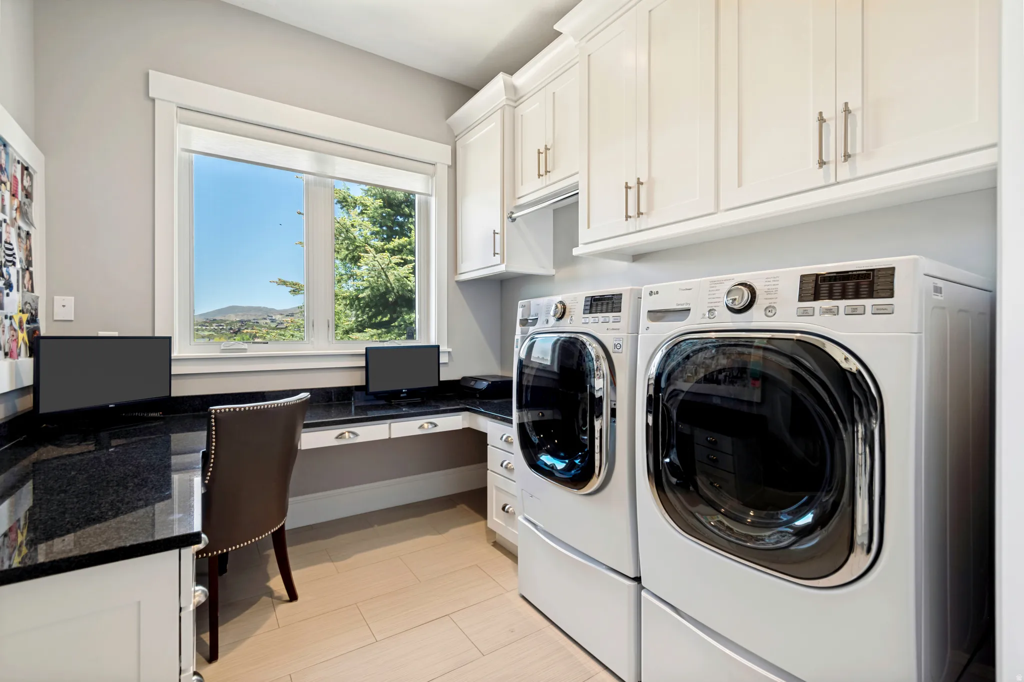 Dedicated laundry area featuring front-loading machines, extensive white cabinetry, and a dark stone countertop with integrated desk space