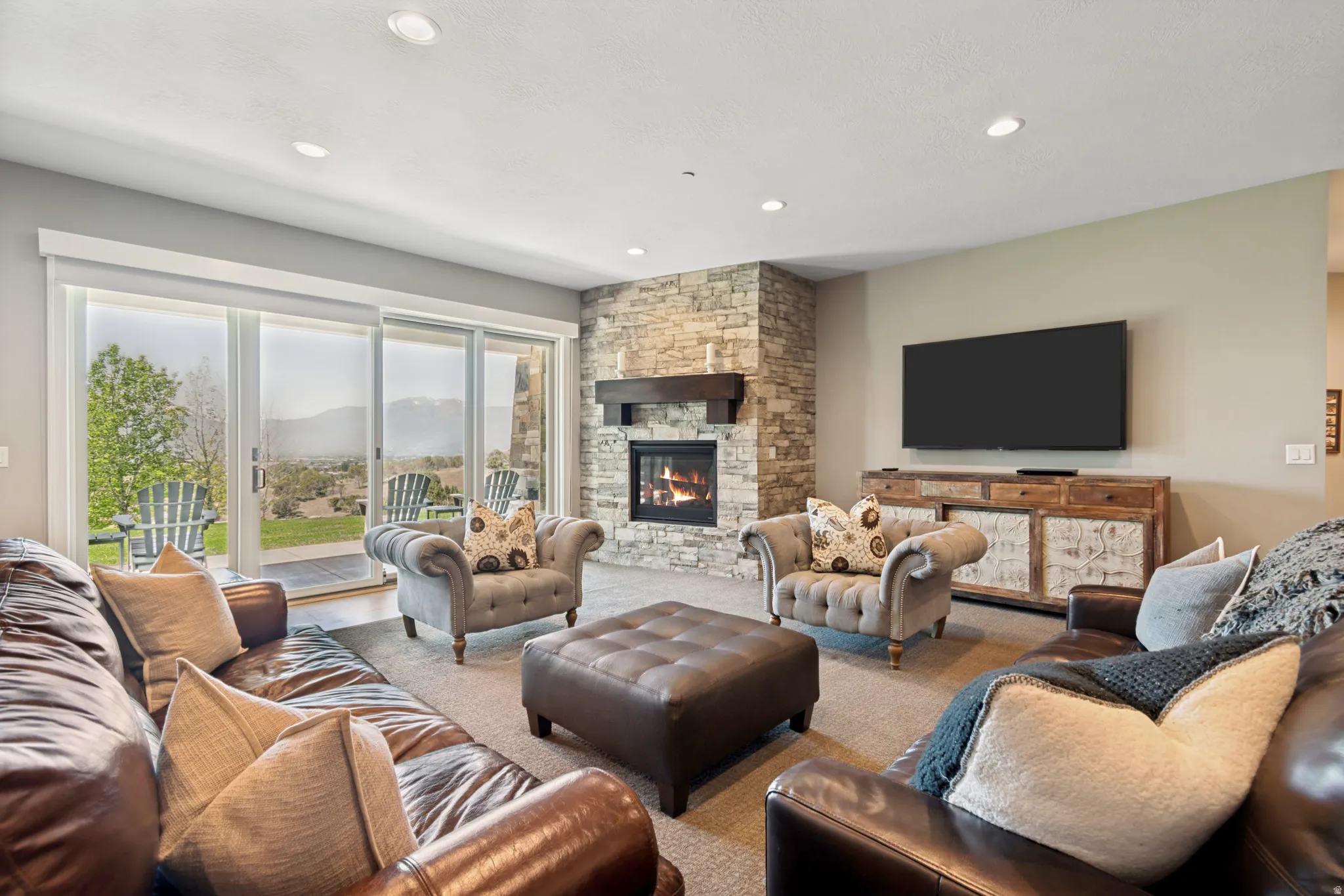 Living area featuring a floor-to-ceiling stacked stone fireplace with a wood-beam mantel, recessed lighting, and a sliding glass door offering outdoor access