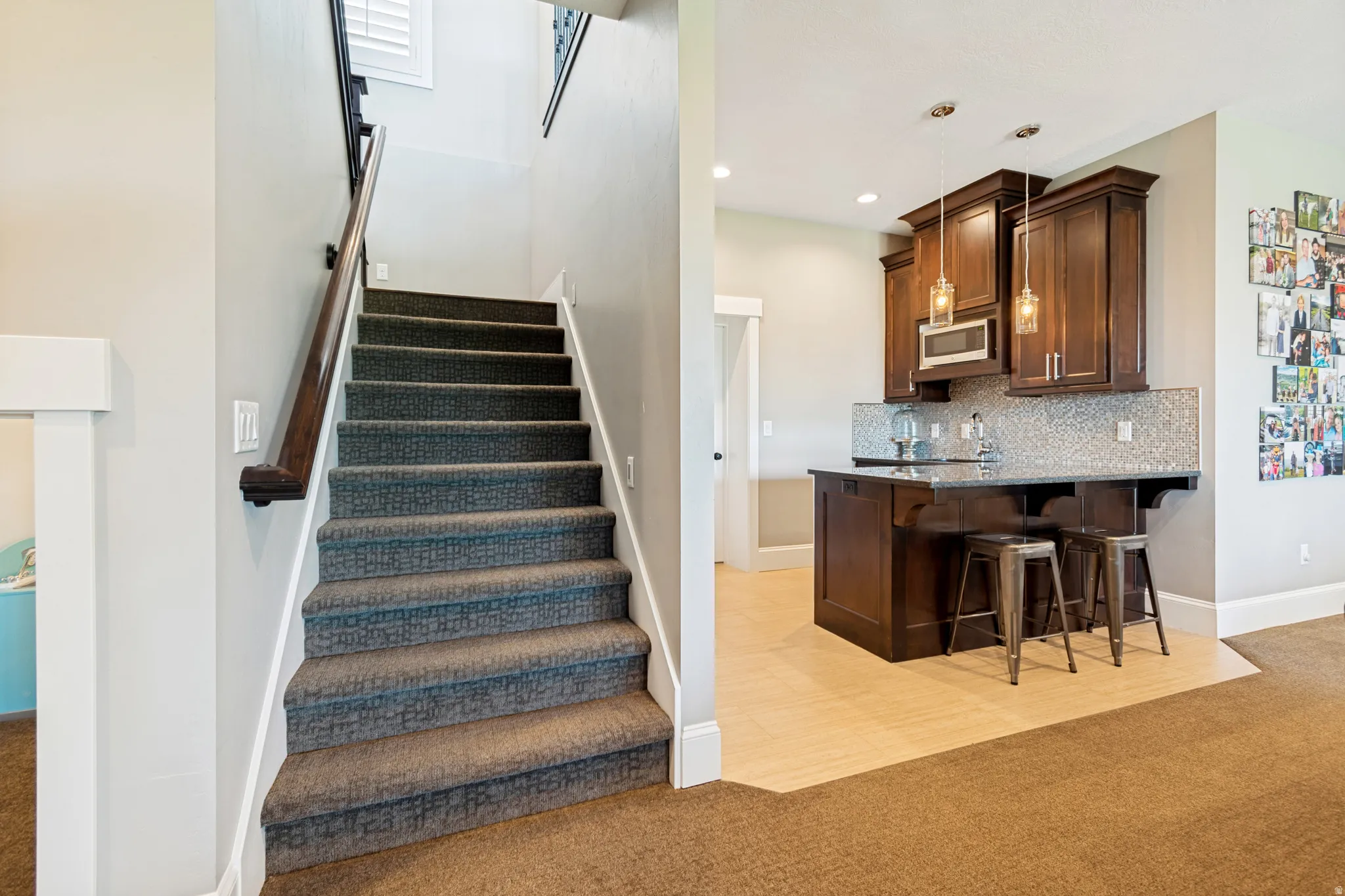 Carpeted staircase with wood handrail, alongside a wet bar featuring dark wood cabinetry, a built-in microwave, and pendant lighting