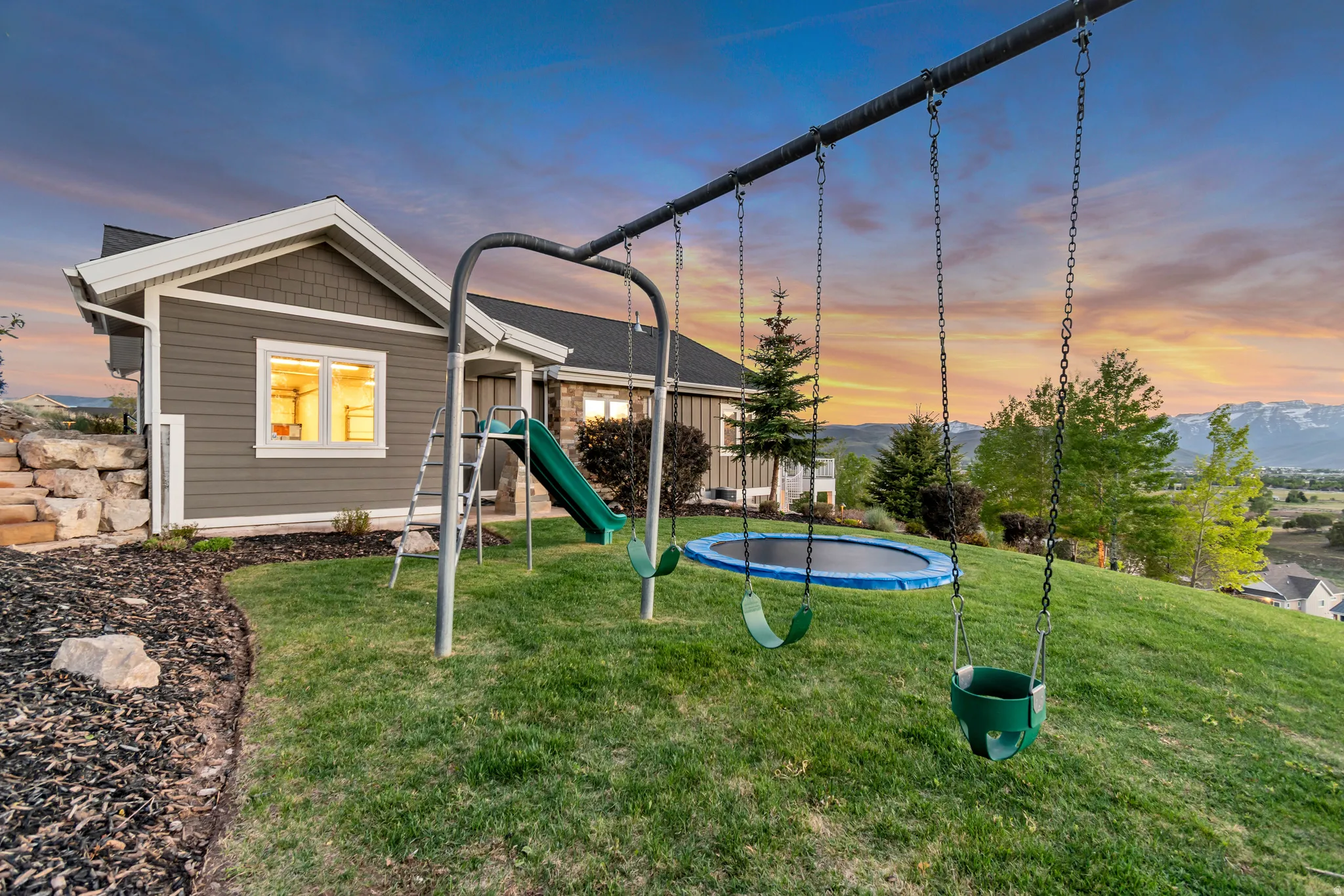 Expansive green lawn with mountain scenery and a residential structure featuring gray siding and white trim
