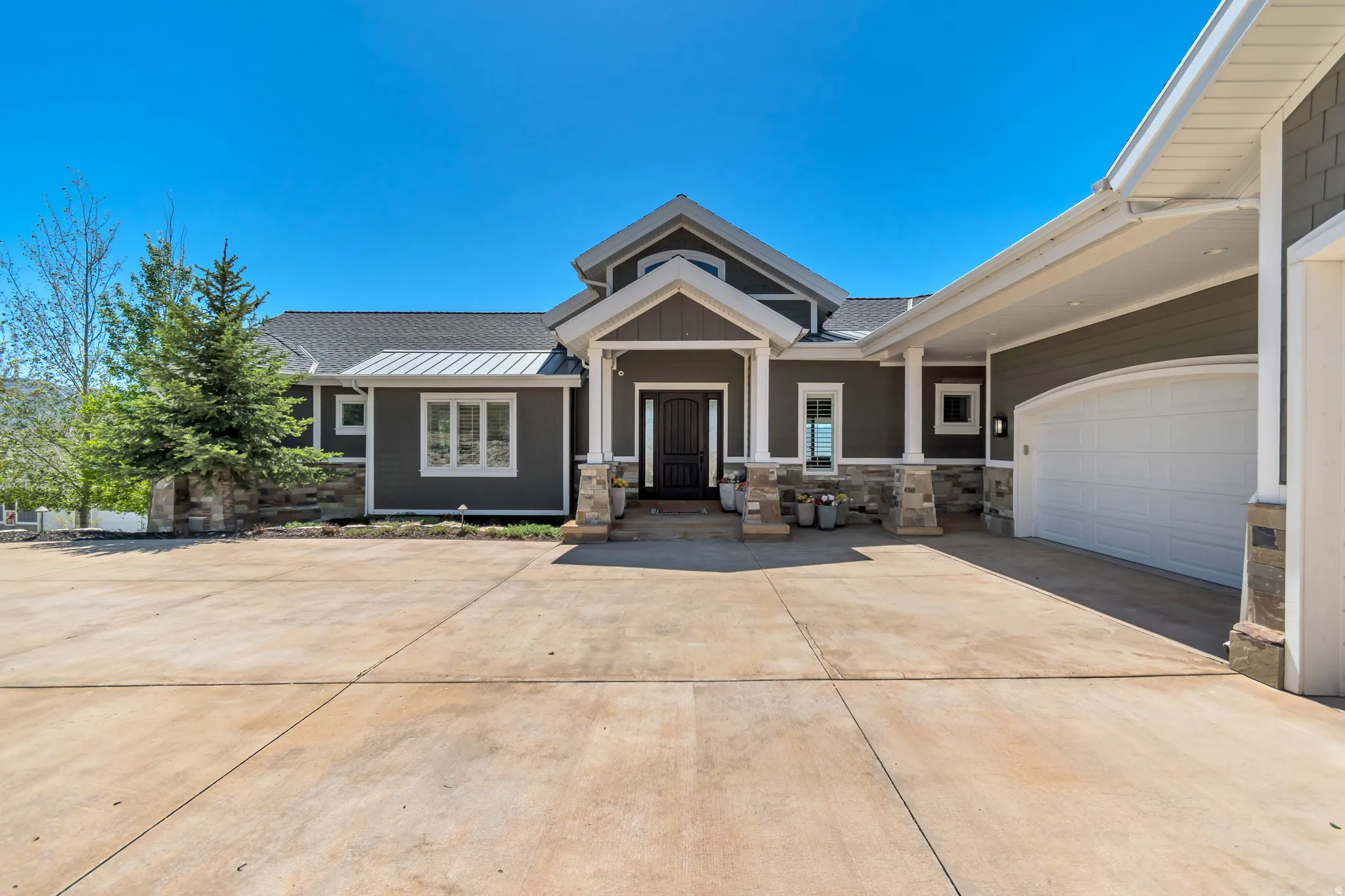 Contemporary exterior featuring dark gray siding with white trim, a covered entryway with stone columns, a dark wood front door, and a two-car garage with an arched white door
