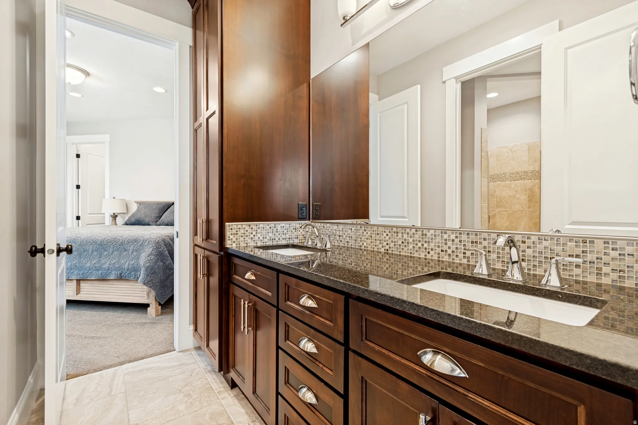 Double vanity featuring dark wood cabinetry, granite-finish countertops, and a tiled backsplash