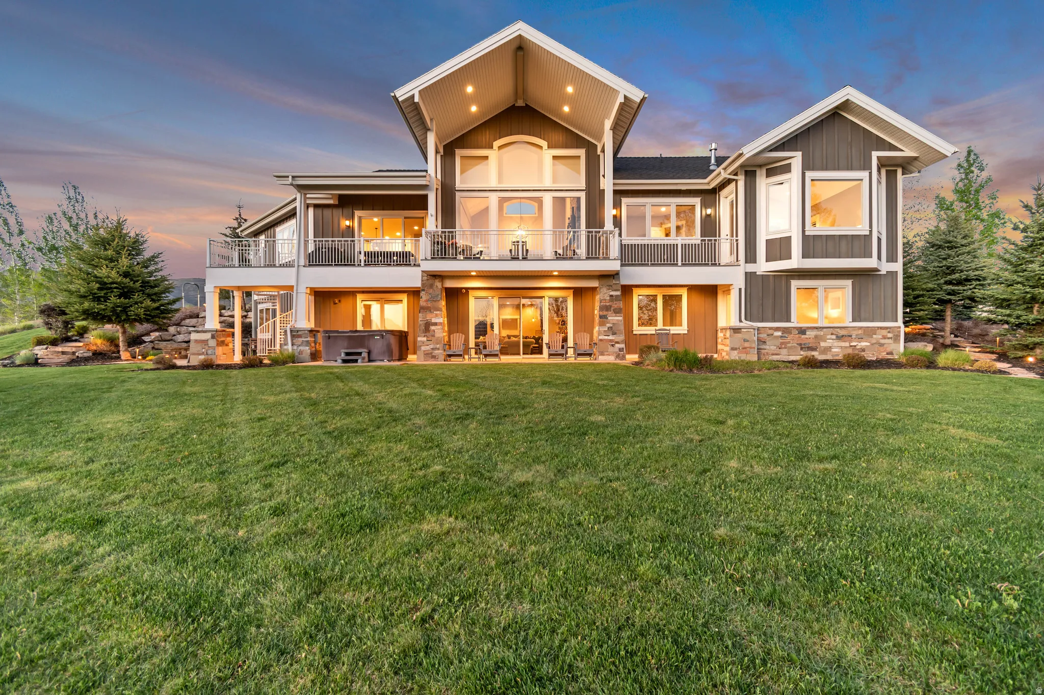 Expansive rear exterior featuring multiple balconies with glass railings, a ground-level patio, and a built-in hot tub