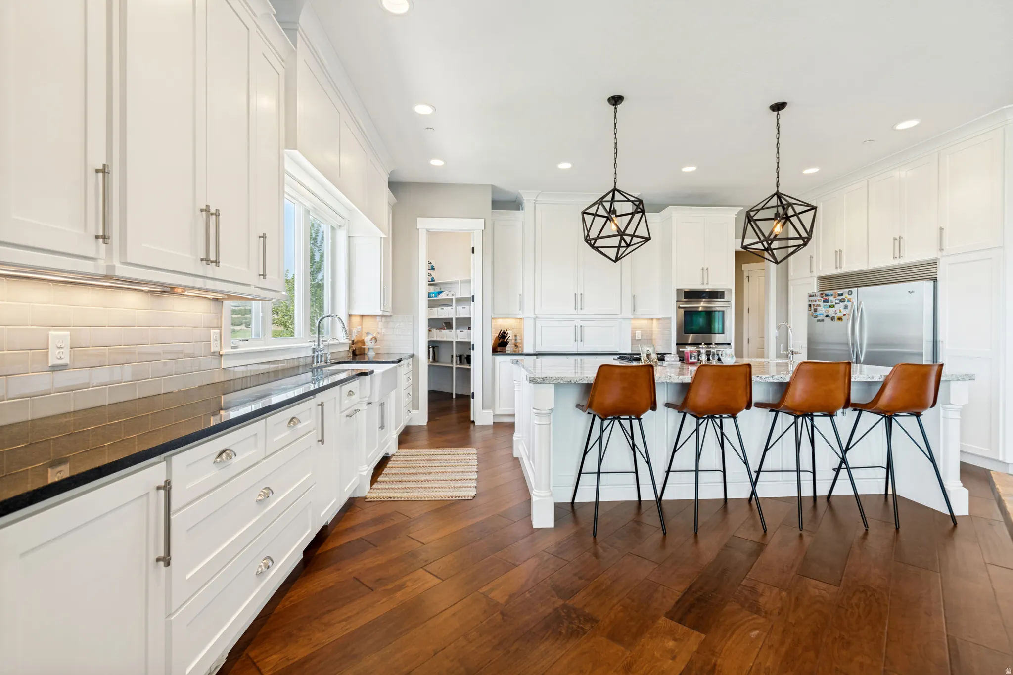Spacious kitchen featuring white cabinetry, dark wood-finish flooring, a kitchen island with seating, stainless steel appliances, and a walk-in pantry