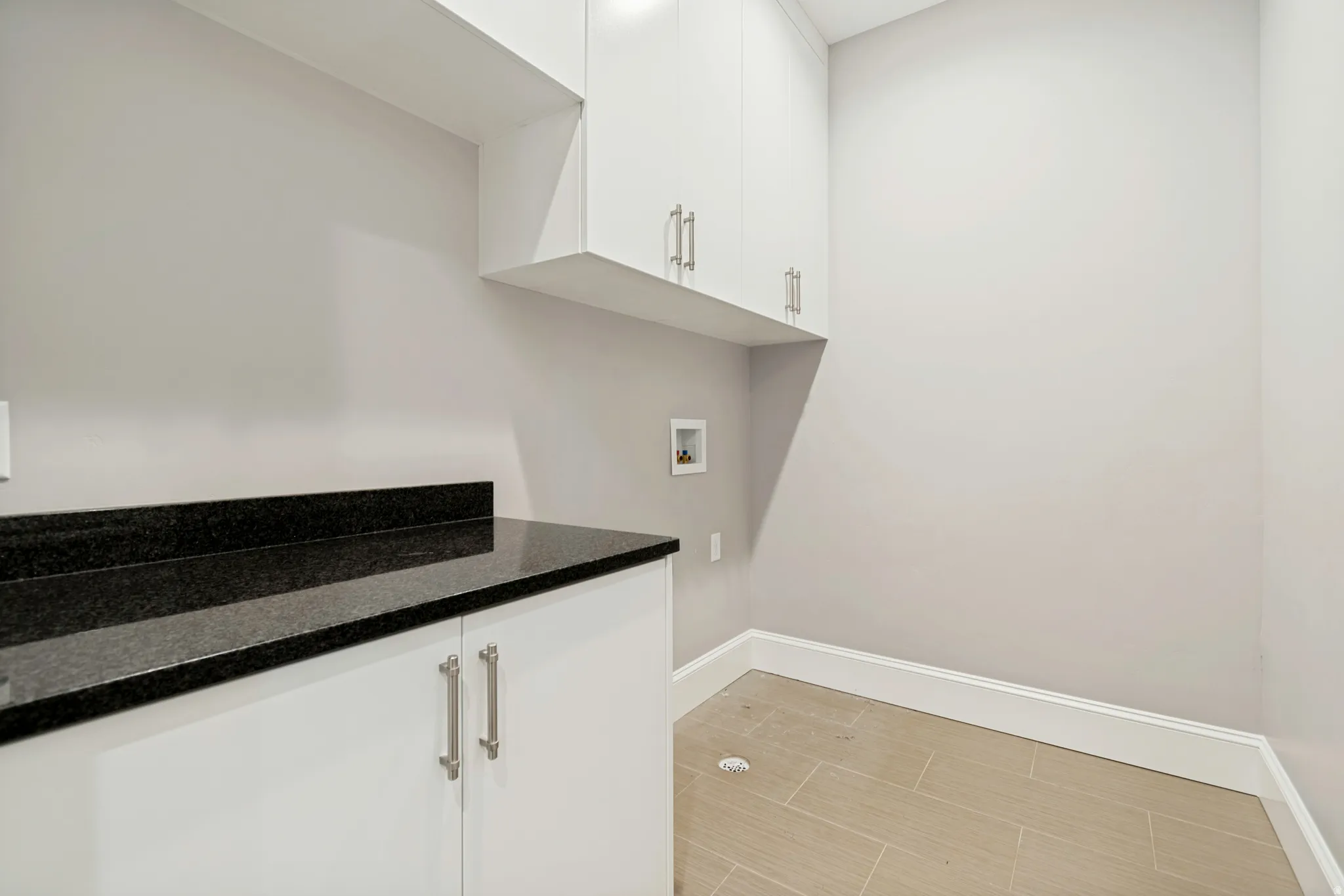 Laundry space featuring white cabinetry, a dark countertop, light-colored tile flooring, and clean baseboards