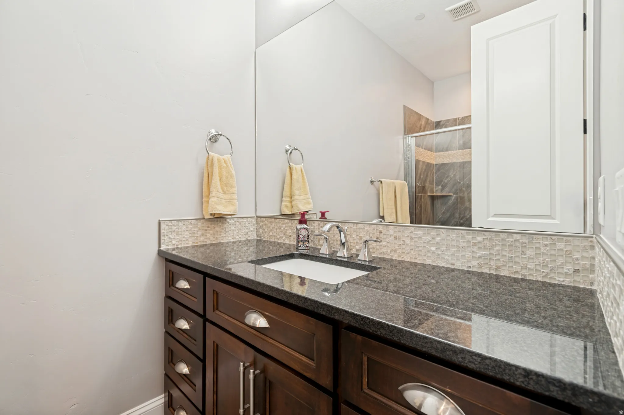 Dark wood-finish vanity with an integrated sink, polished chrome faucet, and dark stone countertop